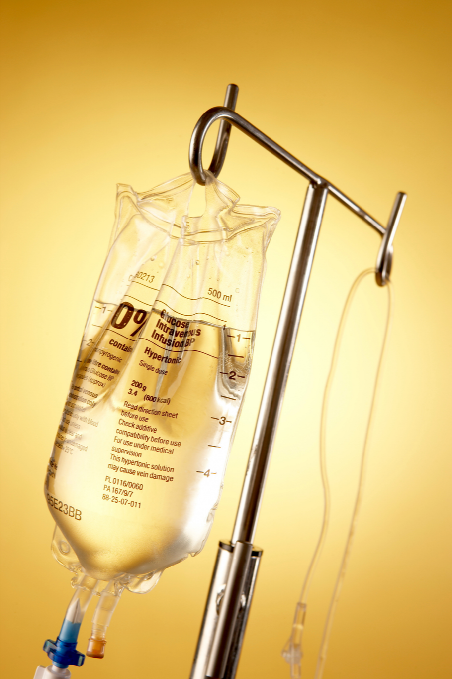 A blood bag hanging from a metal IV stand, filled with clear liquid, against a yellow background.
