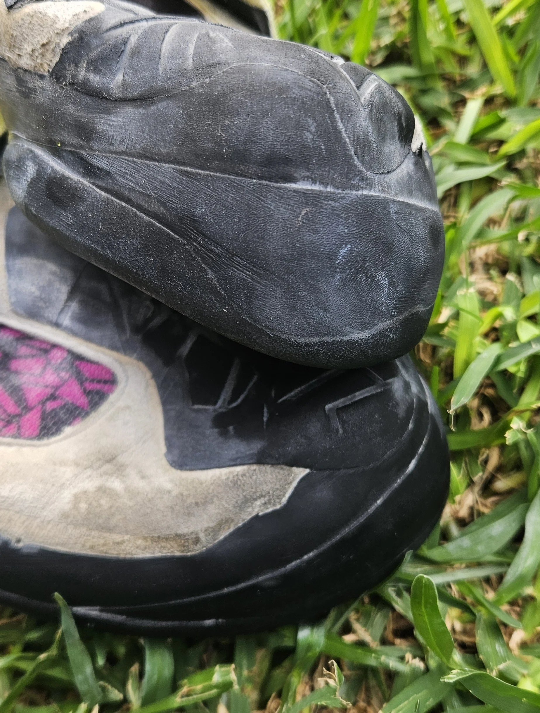 Close-up of black shoe with white sole resting on grass with green blades.