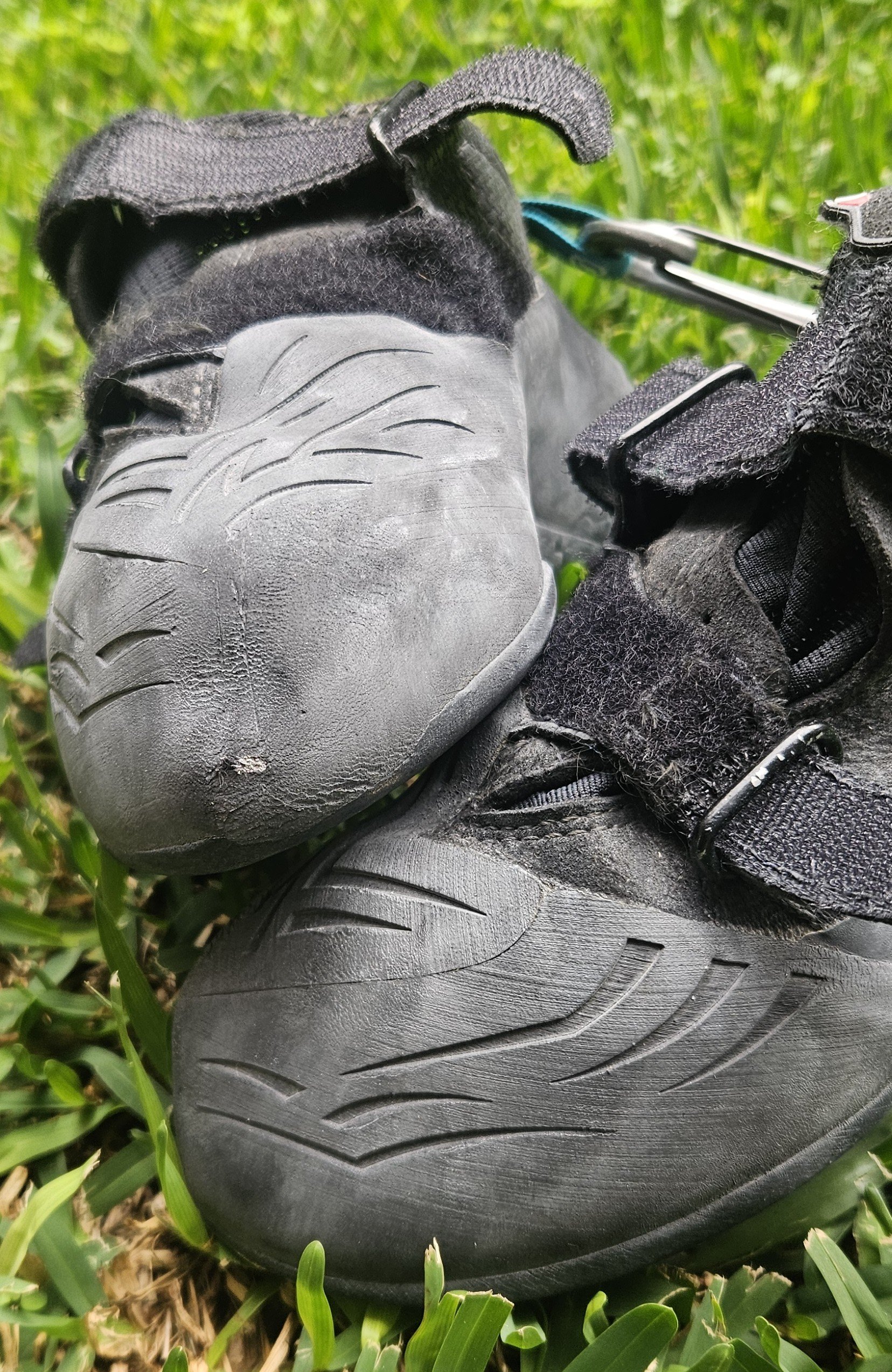 Close-up of a black athletic shoe with a textured sole, placed on green grass.