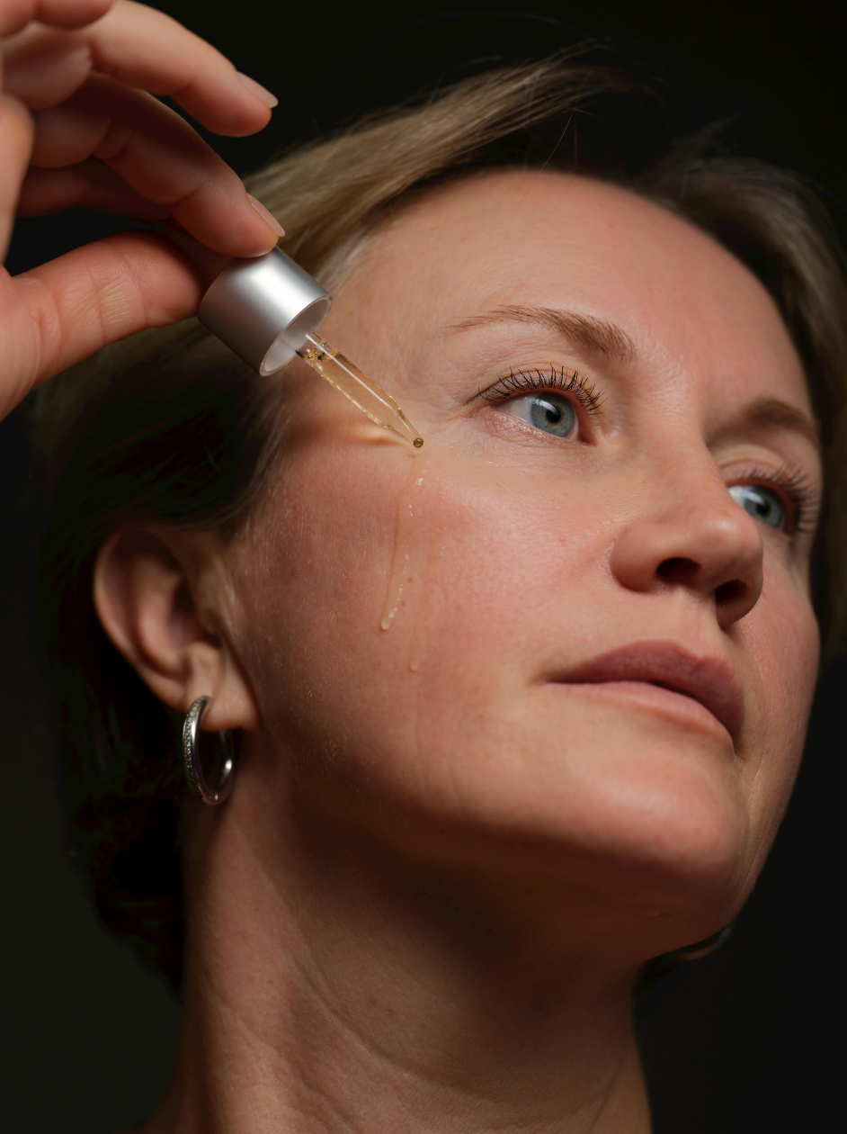 A woman applying a professional skincare serum as part of a home care routine.
