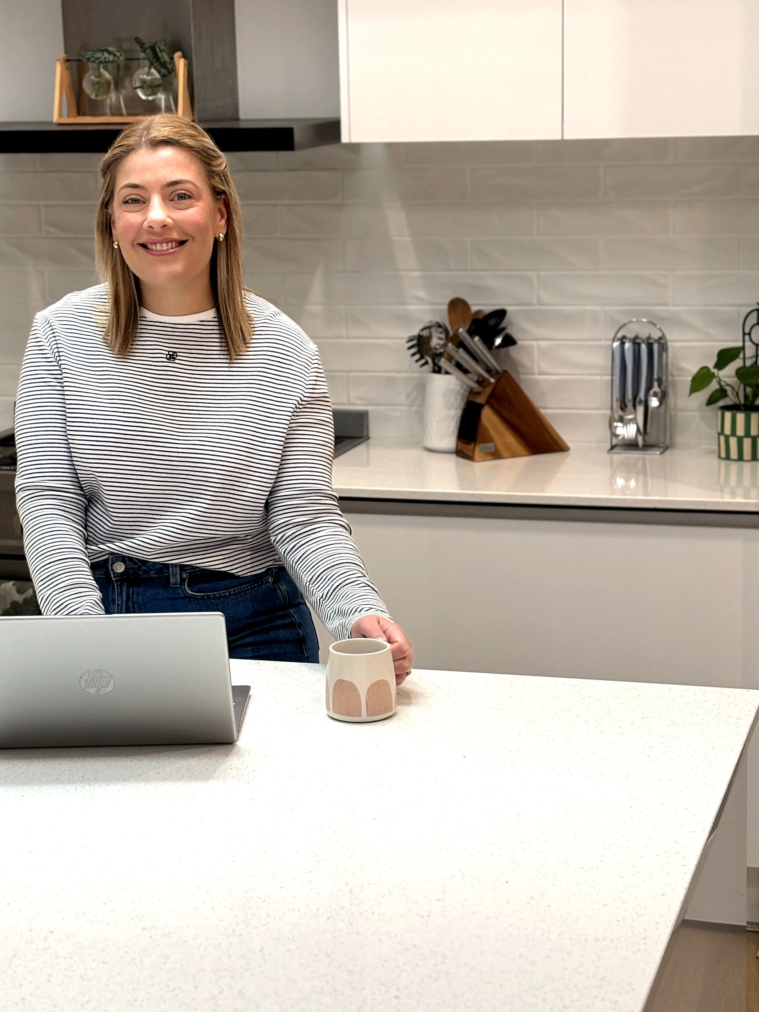 Woman standing in kitchen, with laptop and coffee in hand