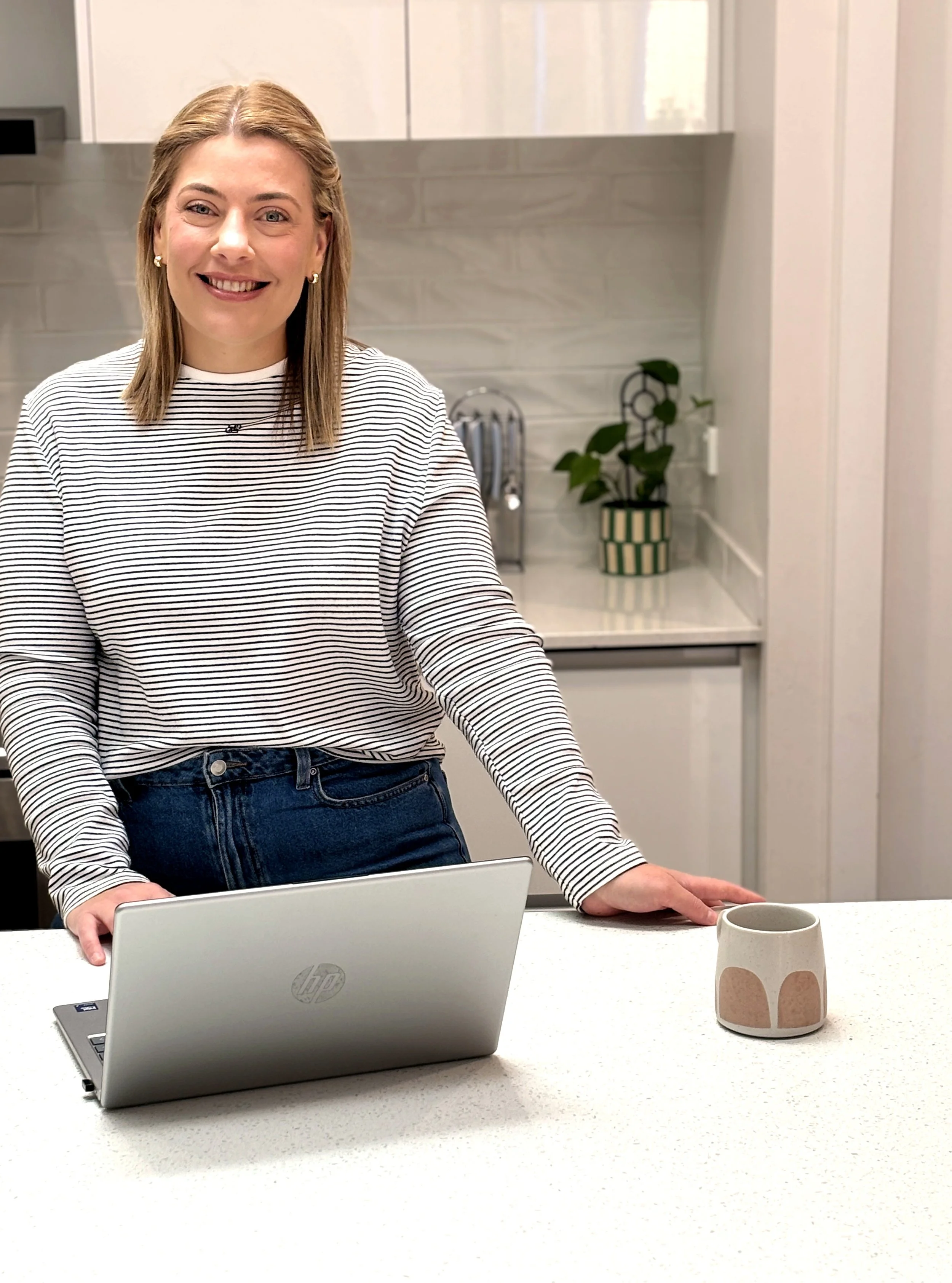 Woman standing in kitchen, with laptop, smiling