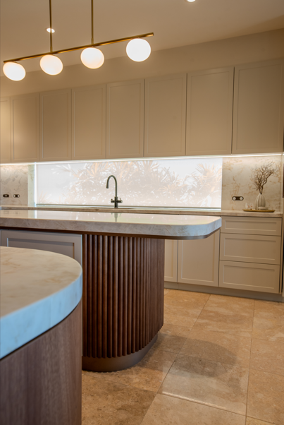 Modern kitchen with beige cabinets, marble countertops, a central island with a wooden base, and a large frosted window above the sink.