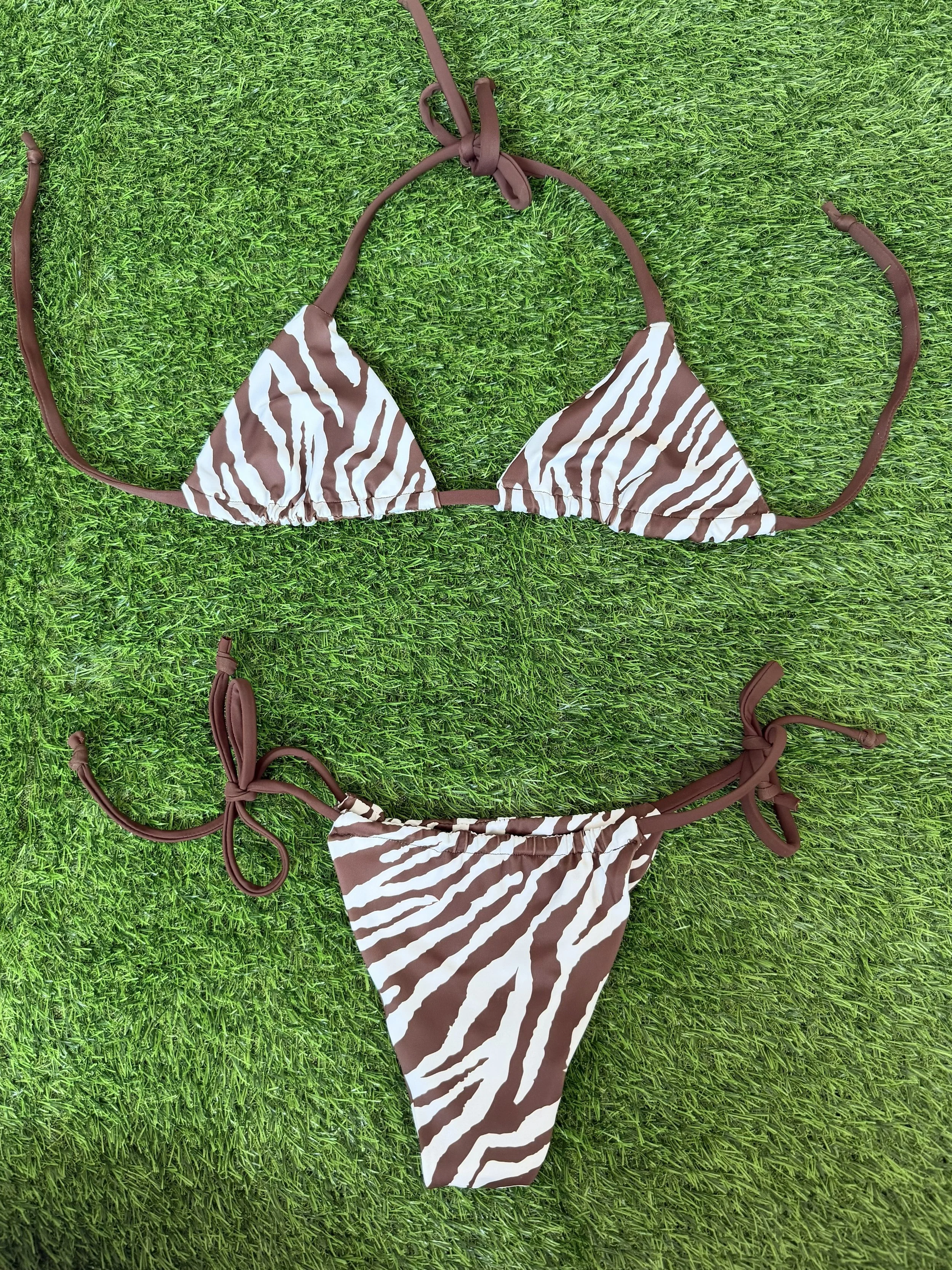 A zebra-print bikini with brown straps lying on green grass.