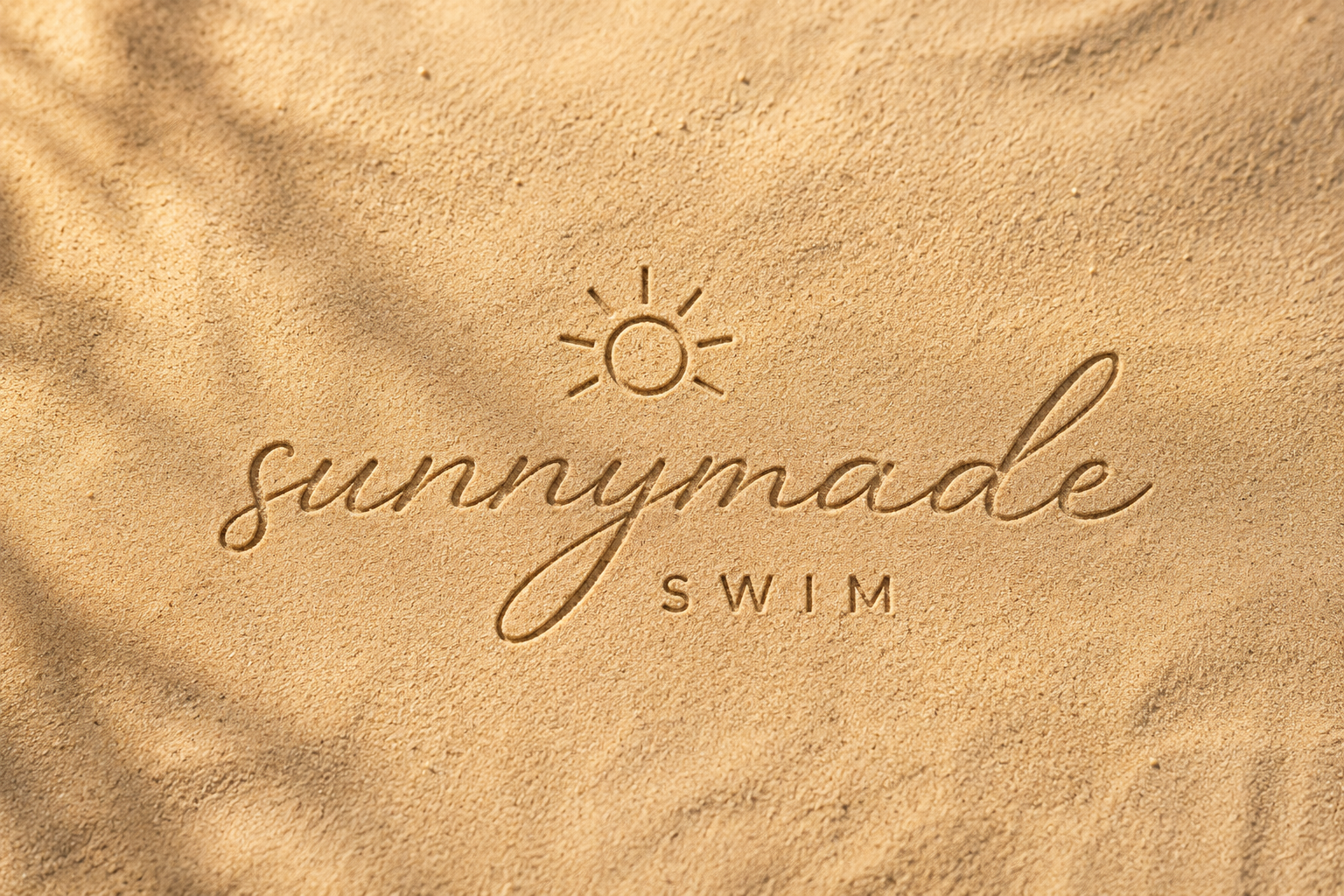 Sand with the words 'summymade SWIM' and a small sun icon inscribed in the sand.