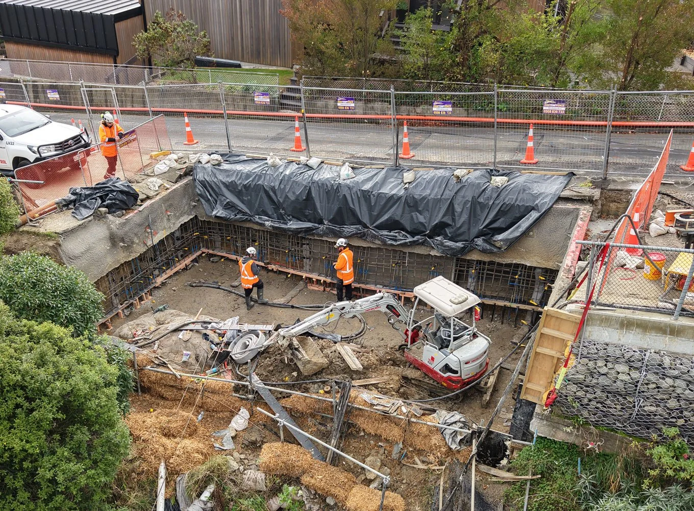 Construction workers and engineers working on an excavation site, with a small excavator digging in the dirt.