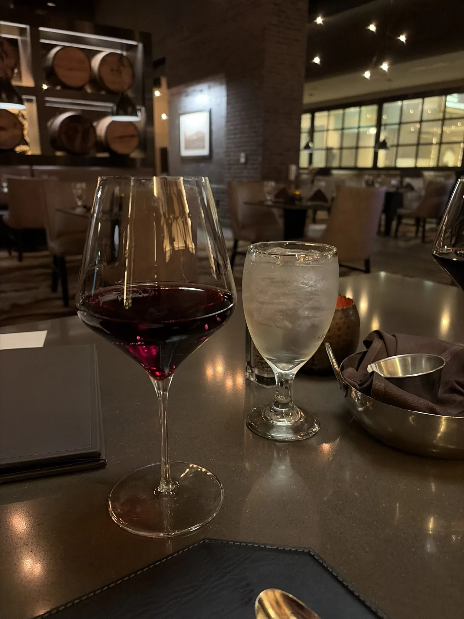 A glass of red wine and a glass of ice water on a restaurant table with dim lighting and a cozy interior.