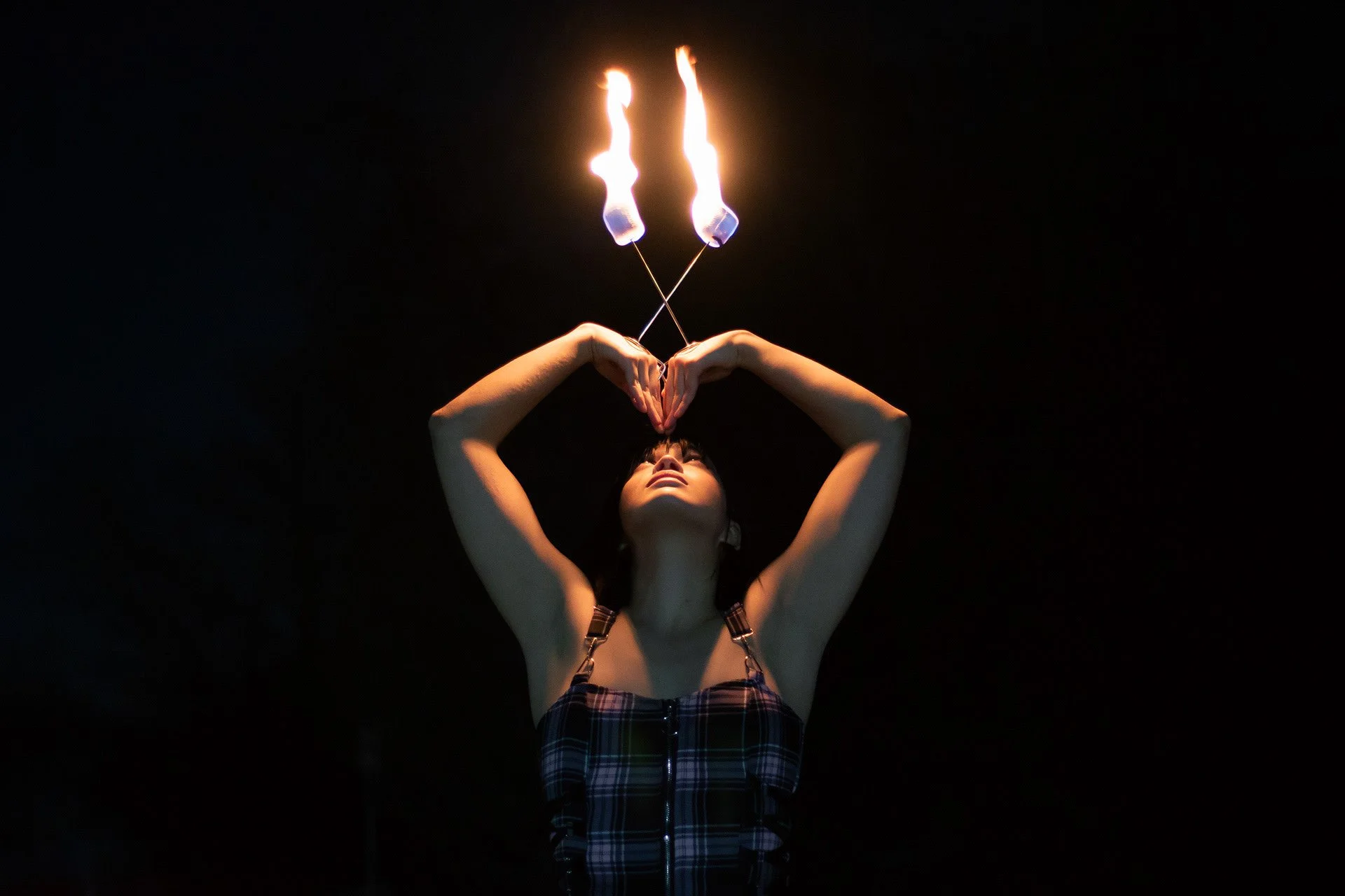A woman spins fire poi in the dark, with flames above her head and her arms raised.