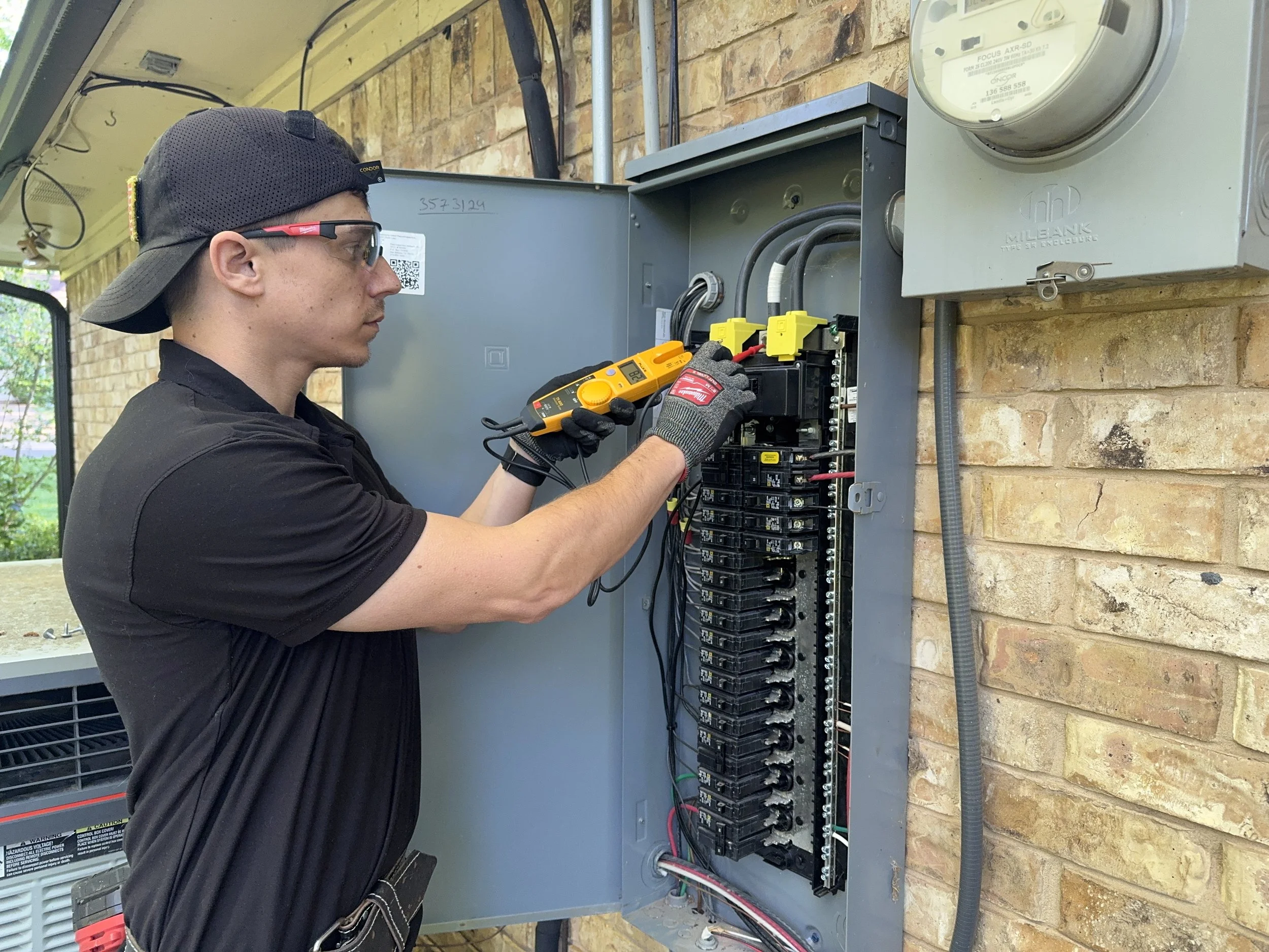 A technician installing or repairing electrical wiring in an outdoor electrical panel on a brick wall, holding a multimeter.