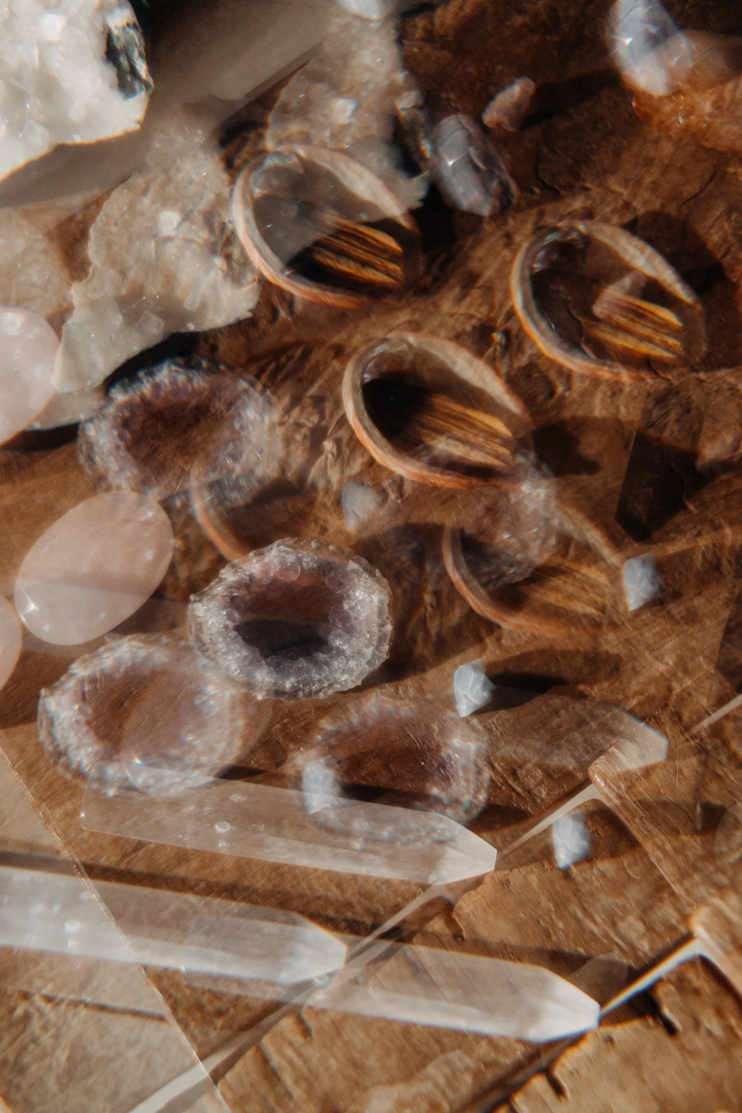 Close-up of various small mineral and crystal specimens, including polished and raw stones, arranged on a wooden surface.