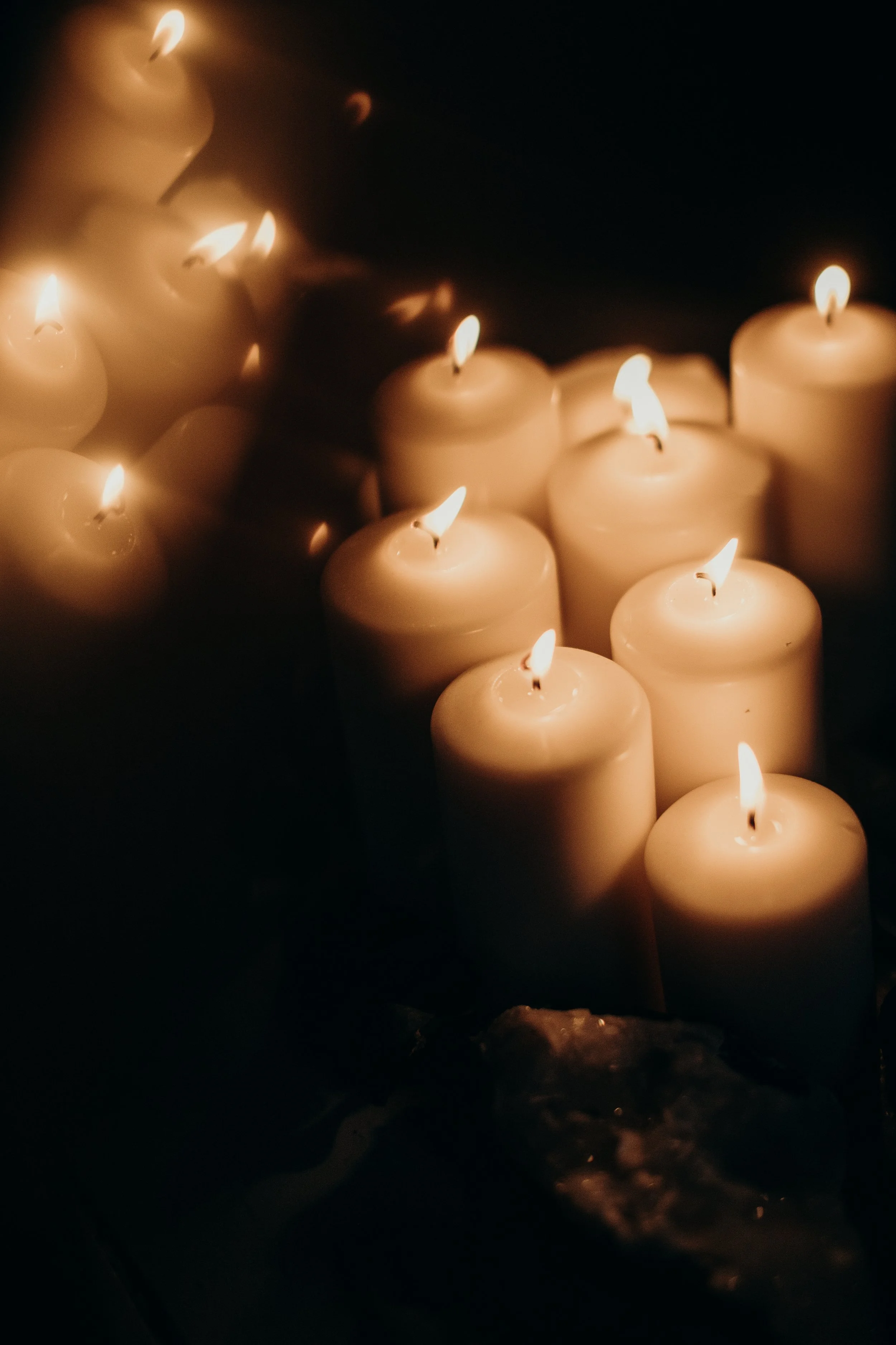Multiple lit white candles in a dark setting, creating a warm glow.