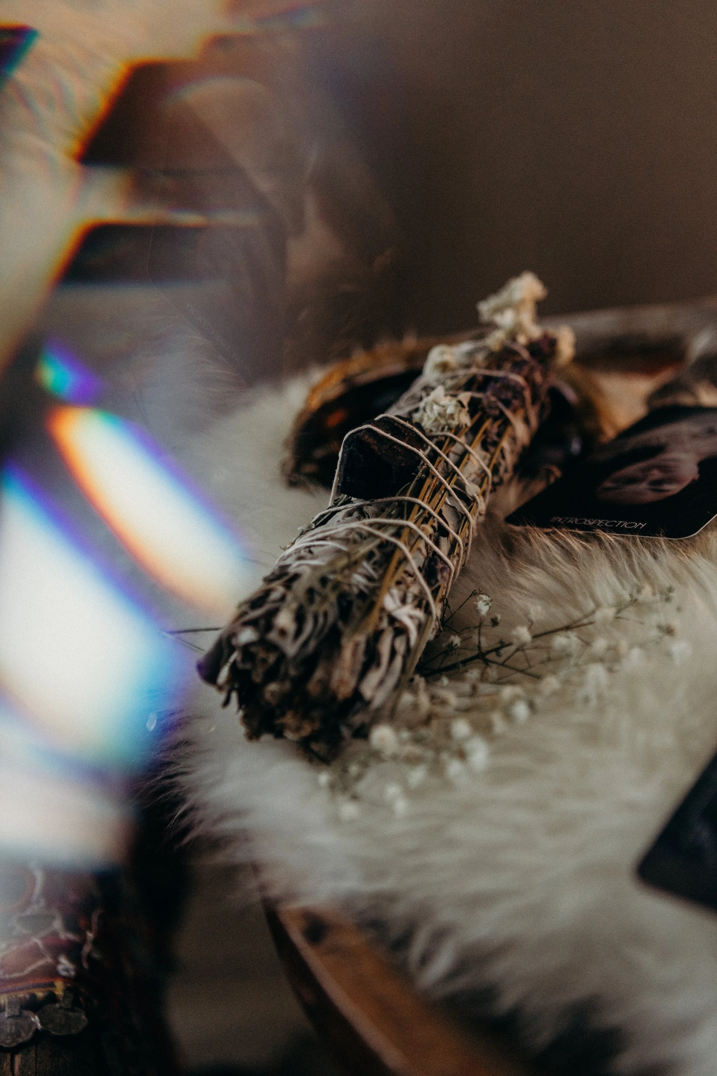 A bundle of herbs tied together with string resting on a fluffy surface, surrounded by dried flowers and a shiny object to the left.