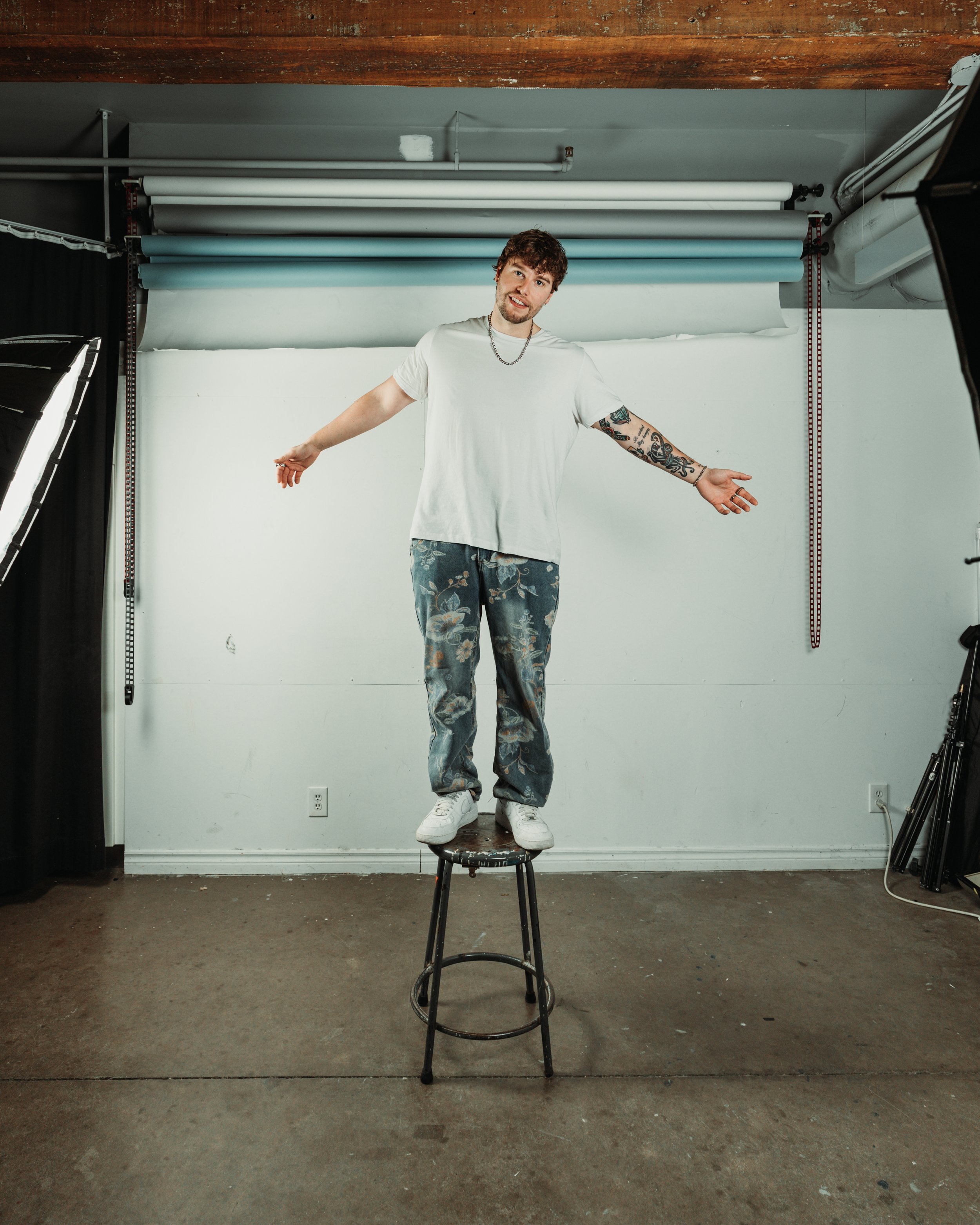 Adam Rodway standing on a chair with his arms out to his side in a studio.