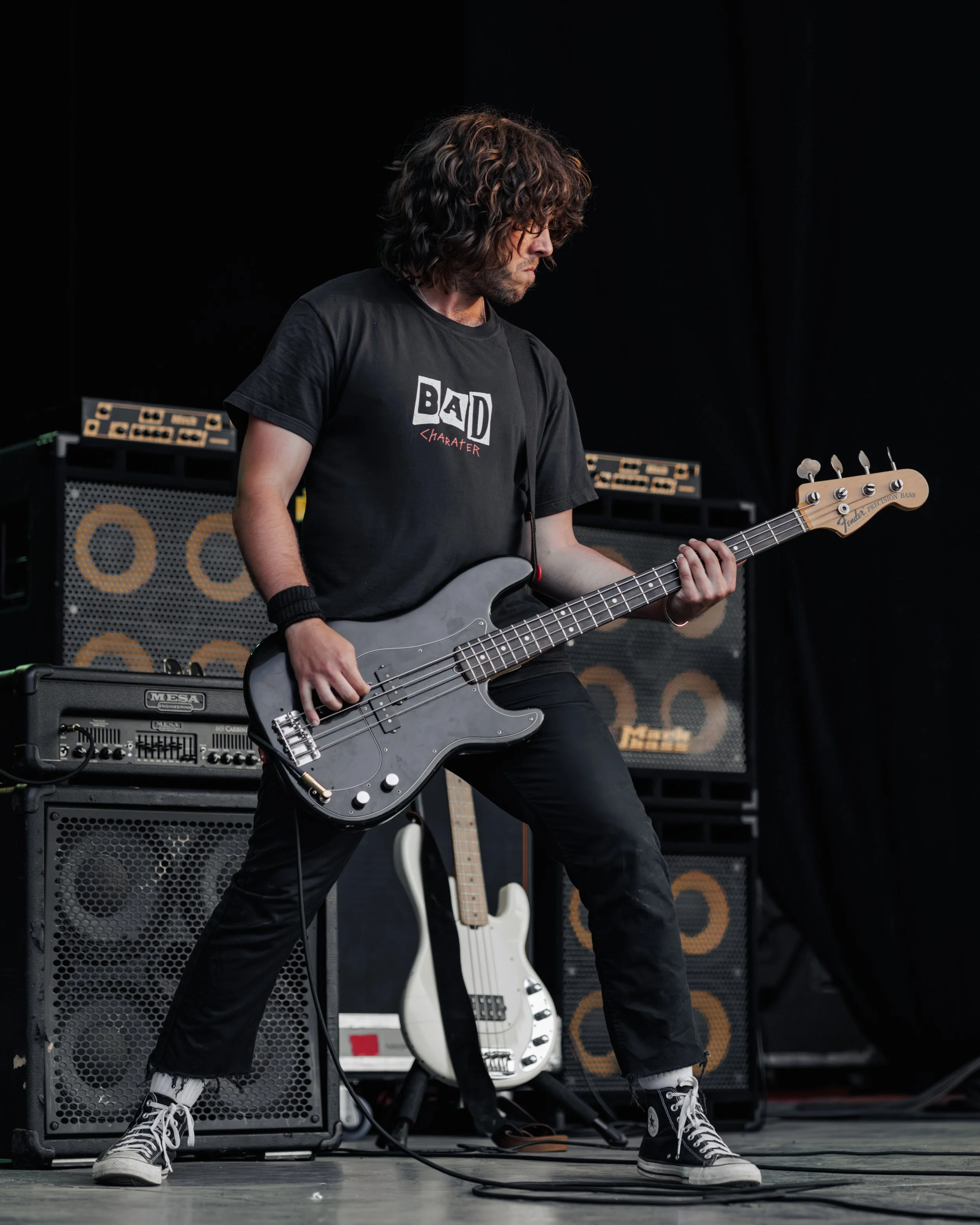 Boris Baker playing bass guitar on stage in front of a stack of amplifiers.