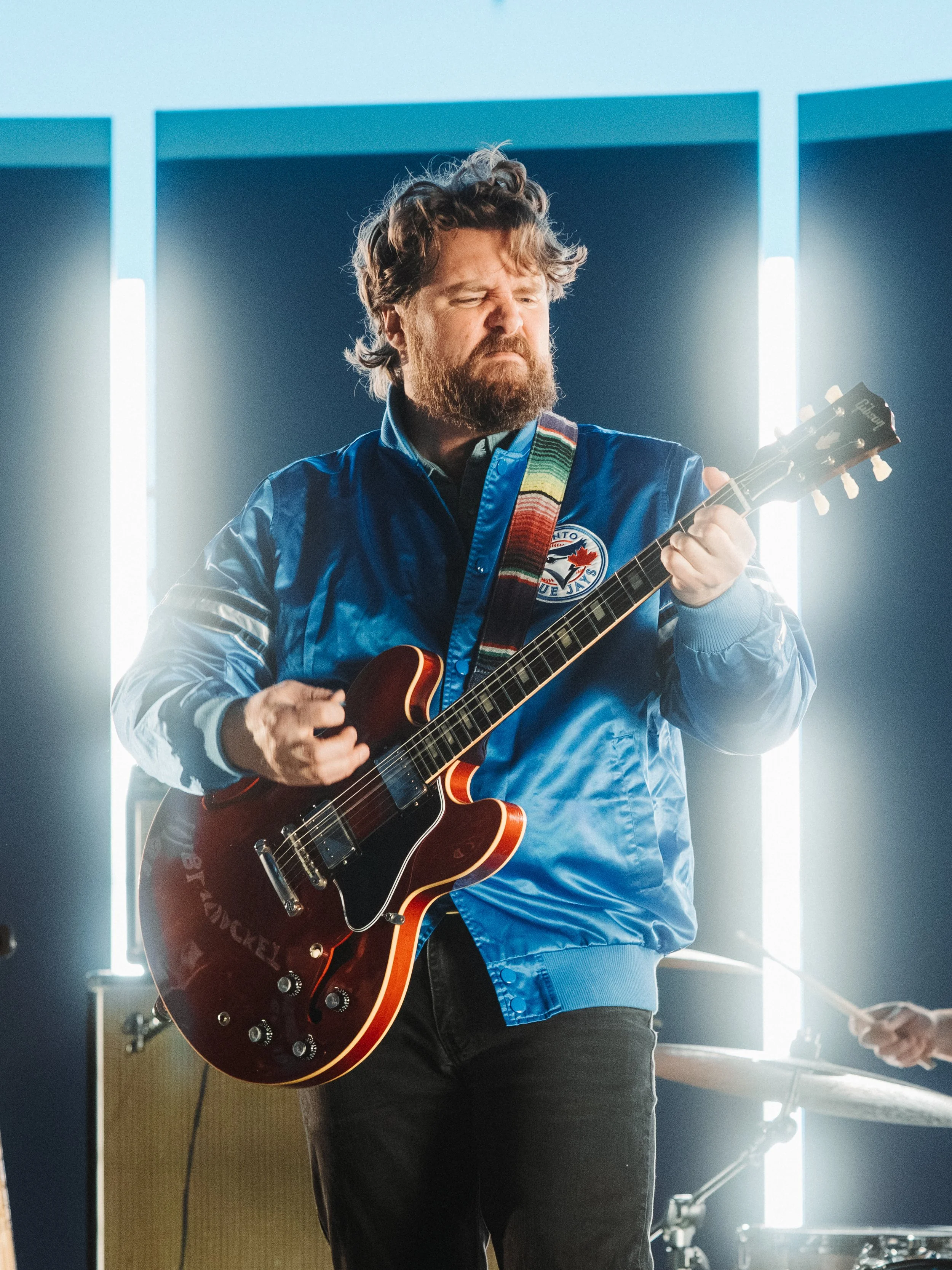 Ewan Currie of The Sheepdogs playing guitar in a Toronto Blue Jay's jacket.