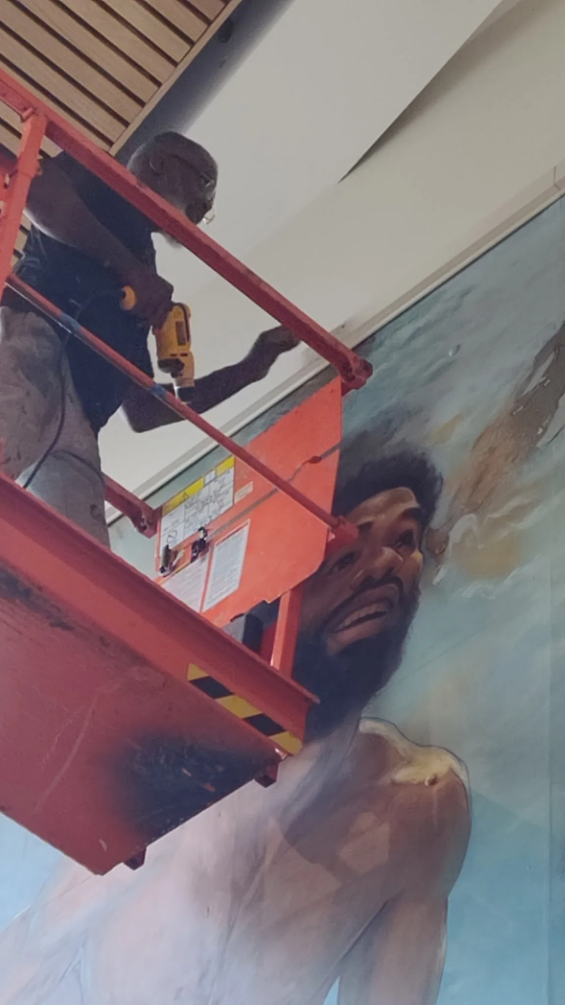 Artist painting a mural of a man with a beard, smiling and shirtless, on a wall.