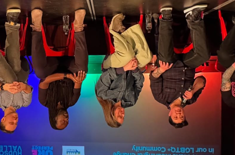 Group of five people seated at a table during a panel discussion or interview, with a colorful background including blue, green, and red lights.