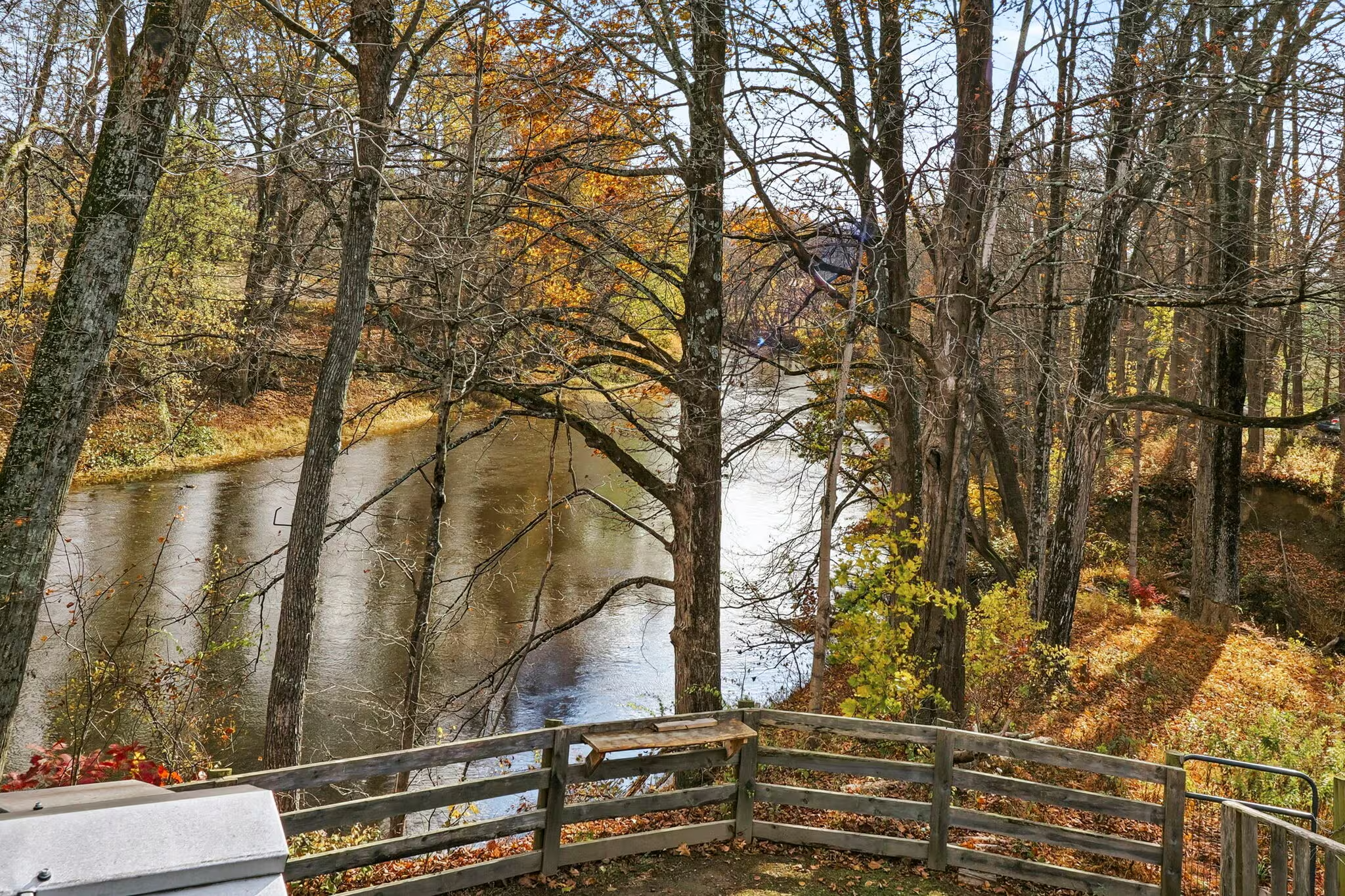 View of a river surrounded by autumn trees with yellow, orange, and brown leaves, and a wooden railing in the foreground.