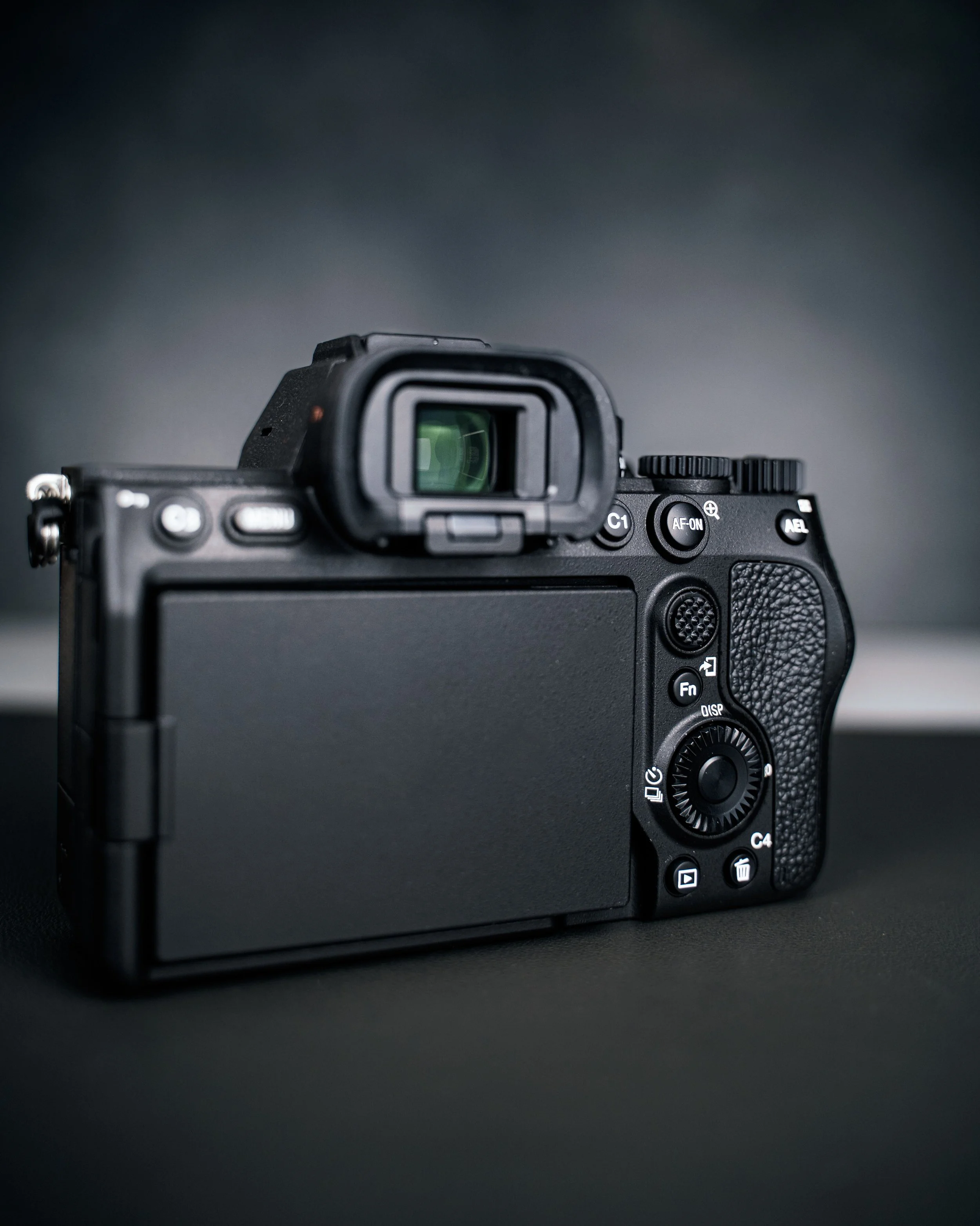 A black digital camera with a large LCD screen on the back and various control buttons, positioned on a black surface with a blurred gradient background.