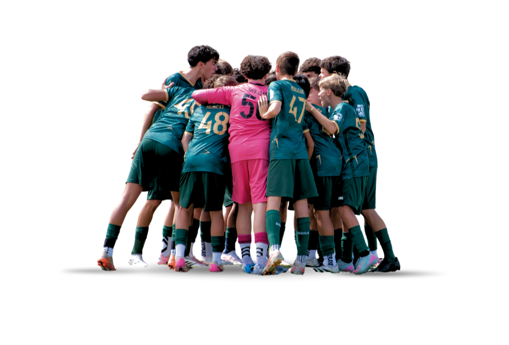 A group of young soccer players huddled together in a team huddle, with one player in a pink goalkeeper jersey, wearing teal uniforms and matching socks.
