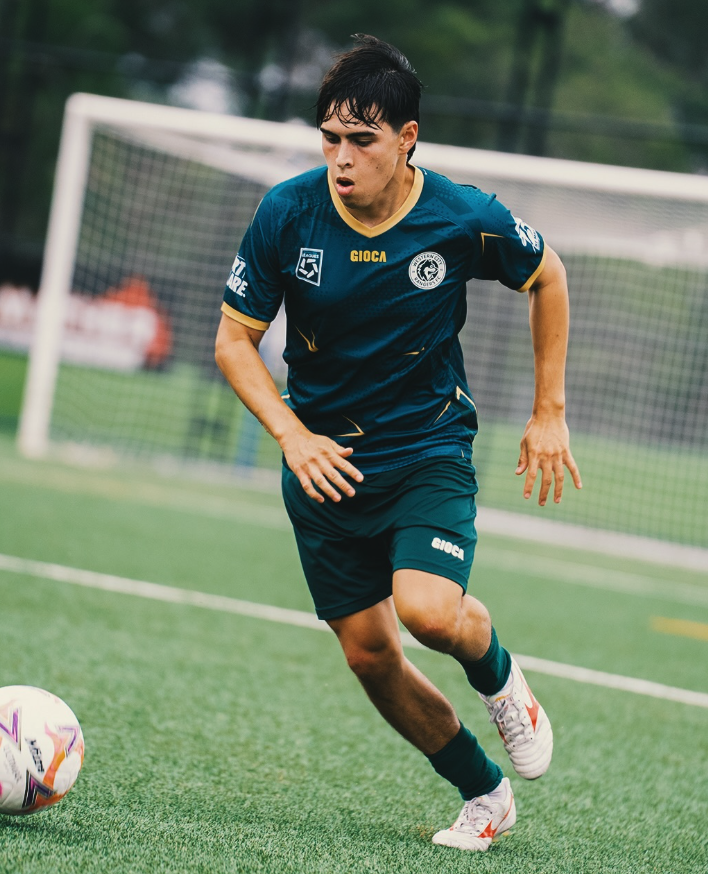 Soccer player in a blue uniform running on the field and approaching the ball in front of the goal.