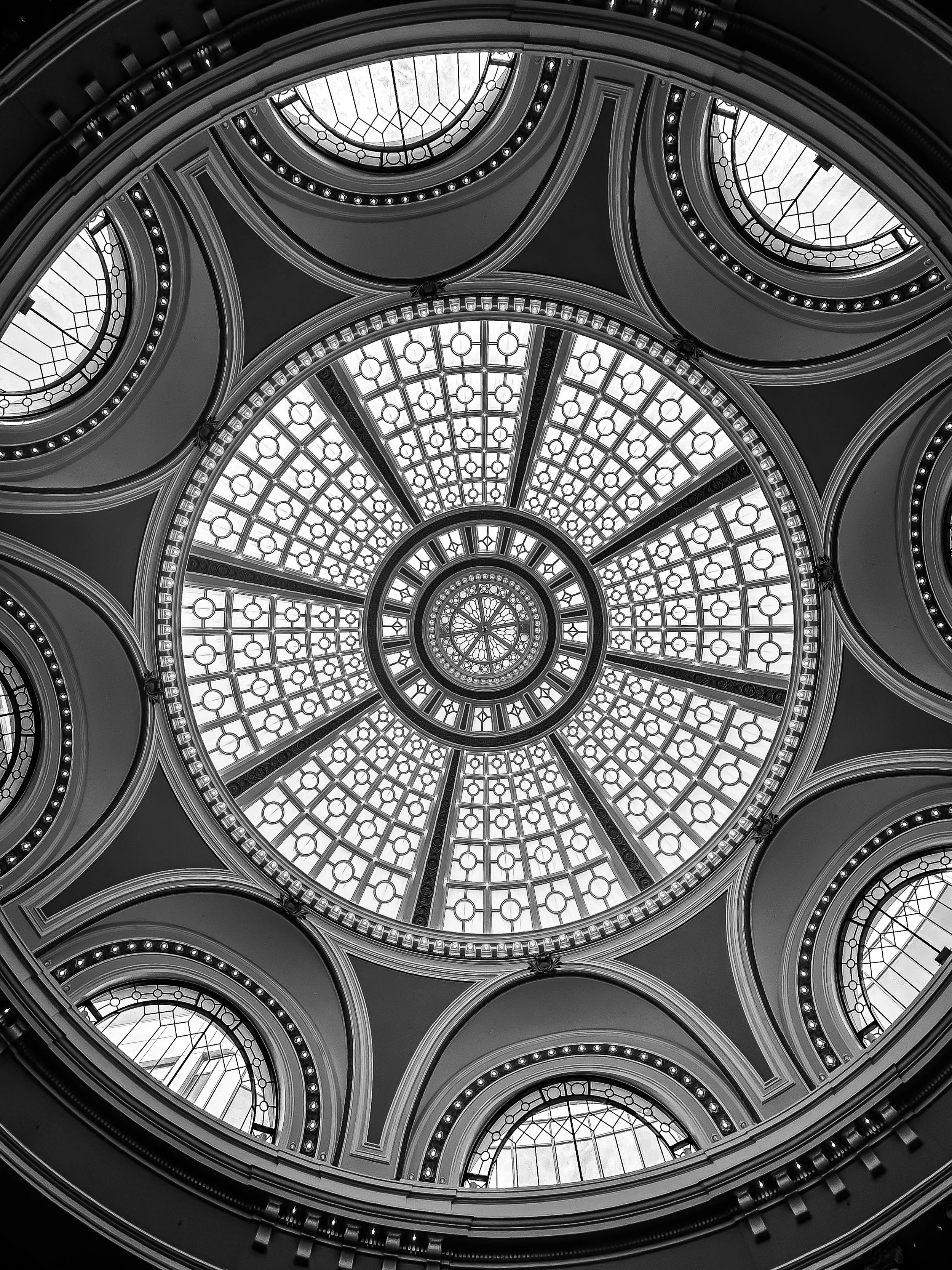 Looking up at a decorative glass dome ceiling with circular windows and intricate metal framing in black and white.
