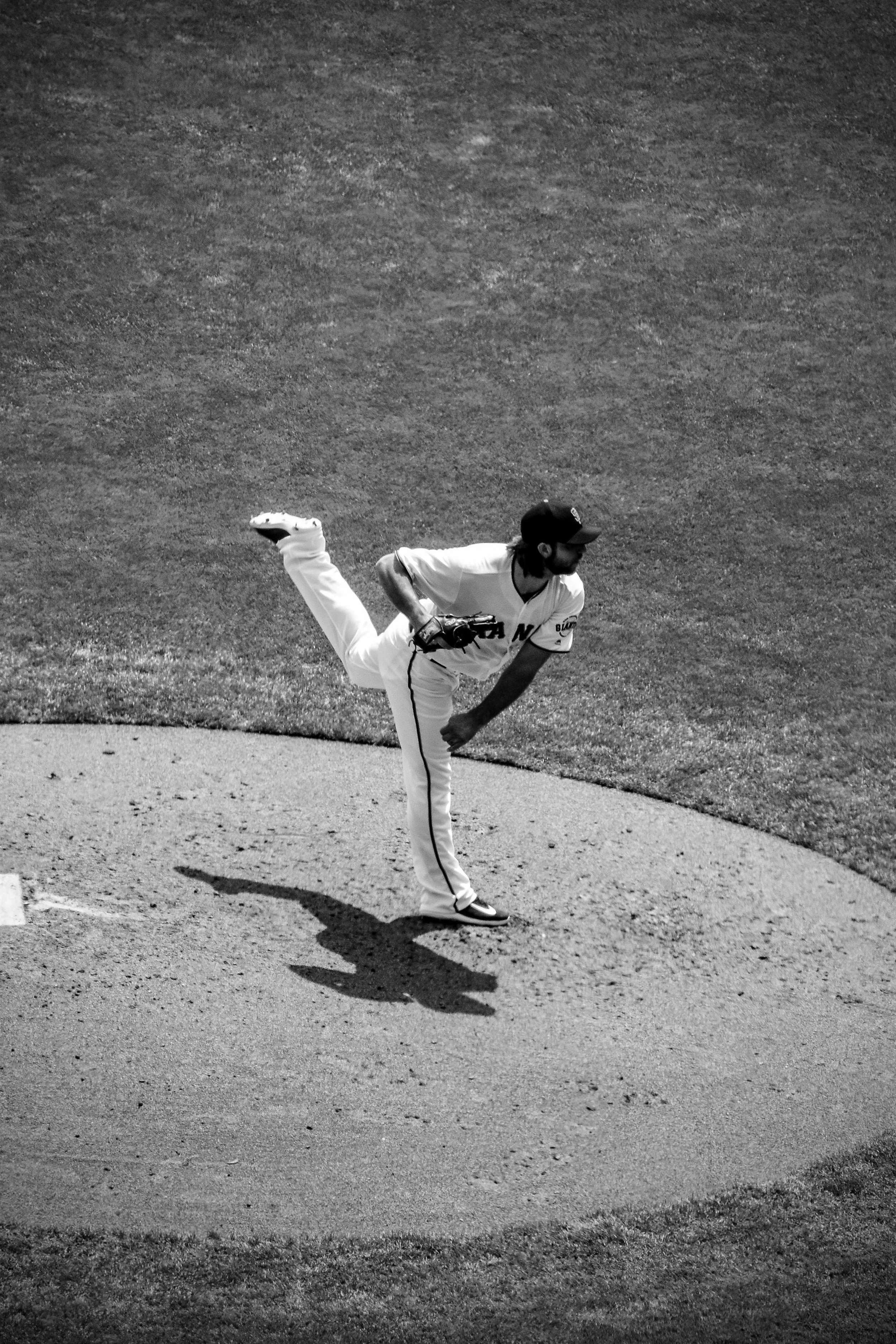 A baseball pitcher in a white uniform throwing a pitch on the mound, casting a shadow on the dirt.