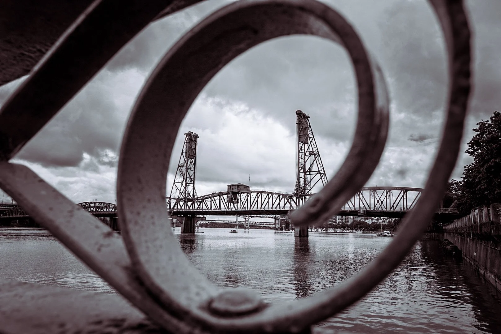 View of a bridge over a body of water, framed by a decorative railing in the foreground, with cloudy sky in the background.
