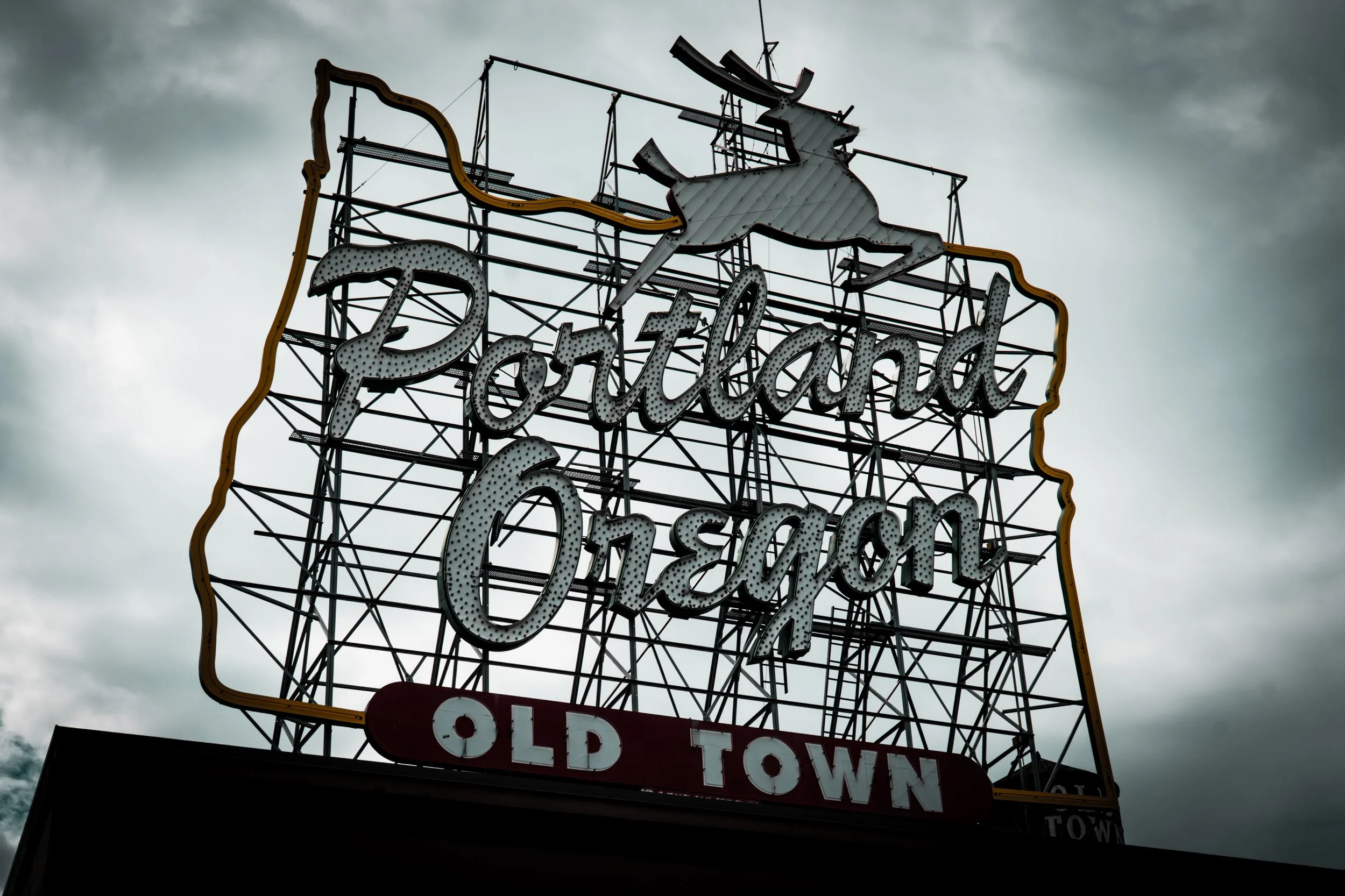 Neon sign for Portland Oregon, featuring a stag and the words "Portland Oregon" with additional text "Old Town" at the bottom, against a cloudy sky.