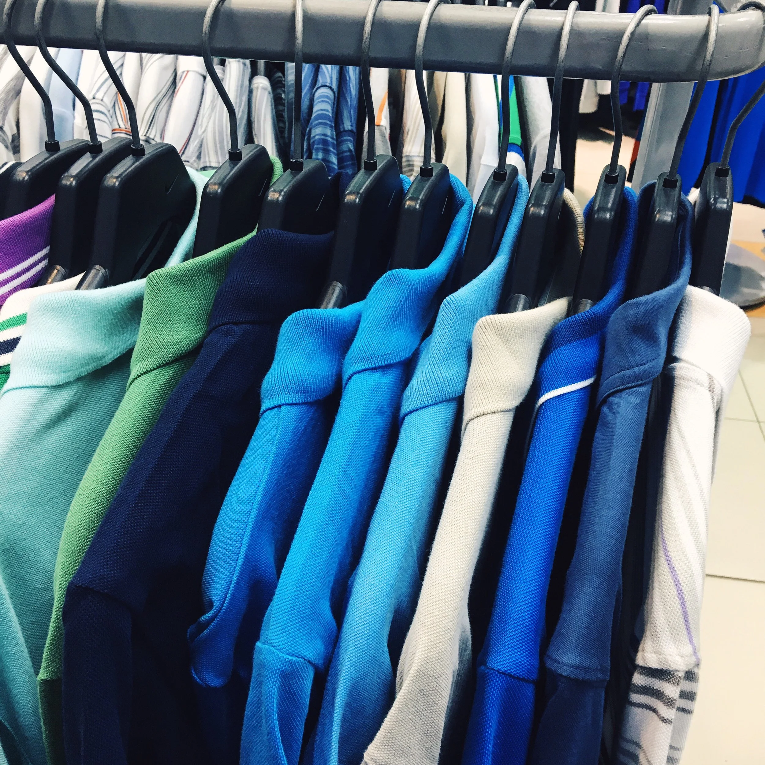 A clothing rack with colorful t-shirts hanging on black plastic hangers in a store.
