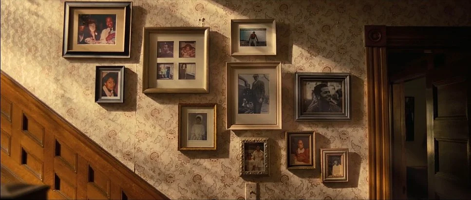 A wall decorated with various framed photographs of different sizes and styles, arranged in a collage pattern above a wooden staircase.