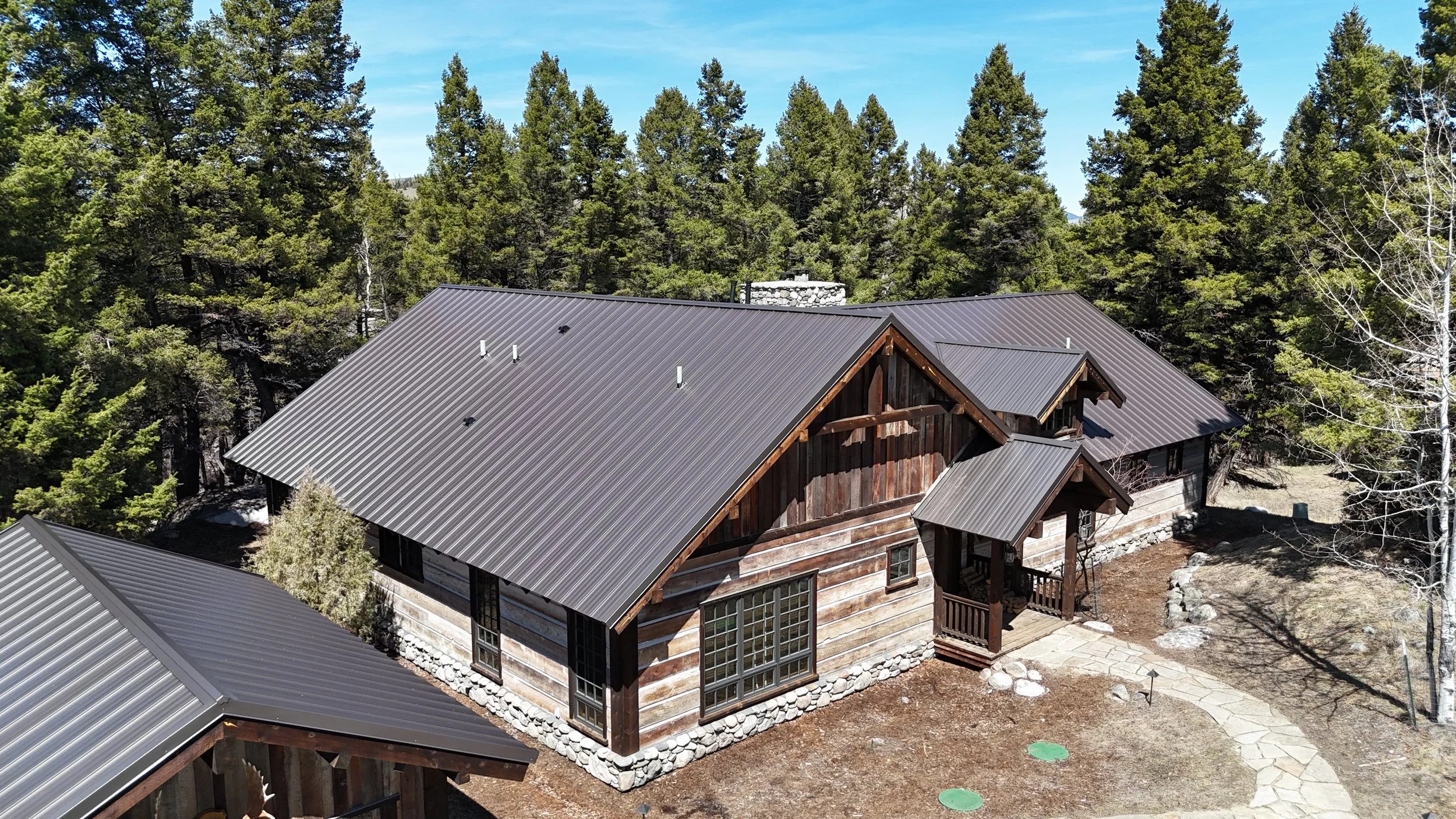 Aerial view of a rustic house with a metal roof surrounded by trees and a stone pathway.