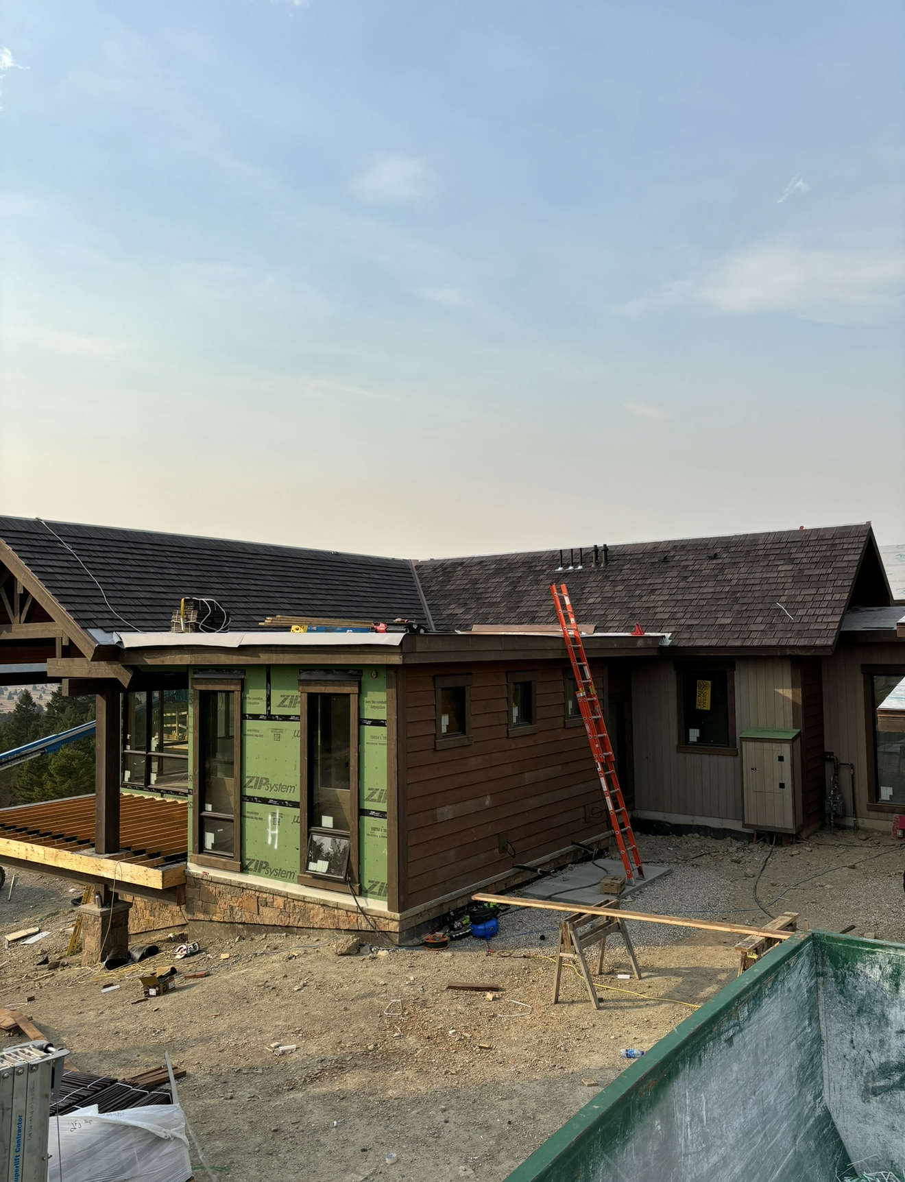 Construction site with a partially built house, a red ladder leaning against the wall, construction tools on the ground, and a clear sky overhead.