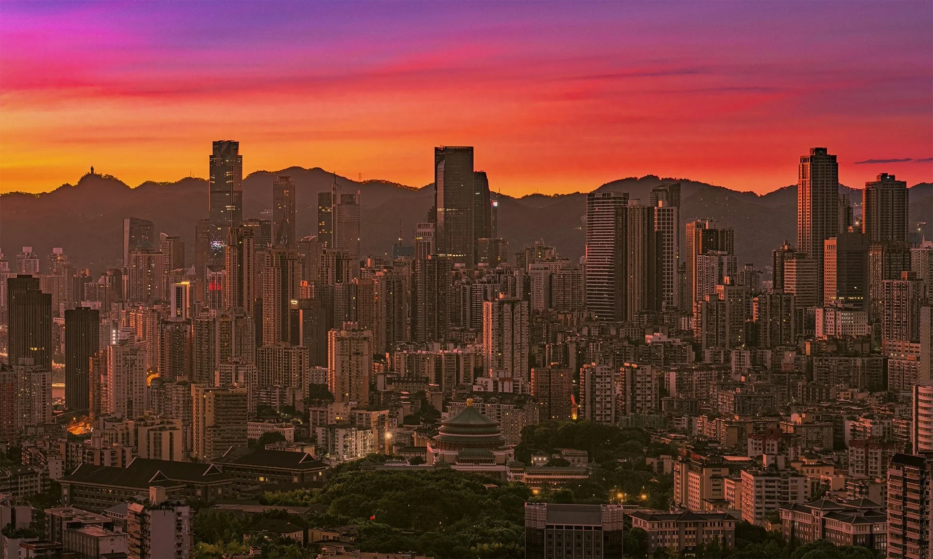 City skyline at sunset with skyscrapers and mountains in the background.