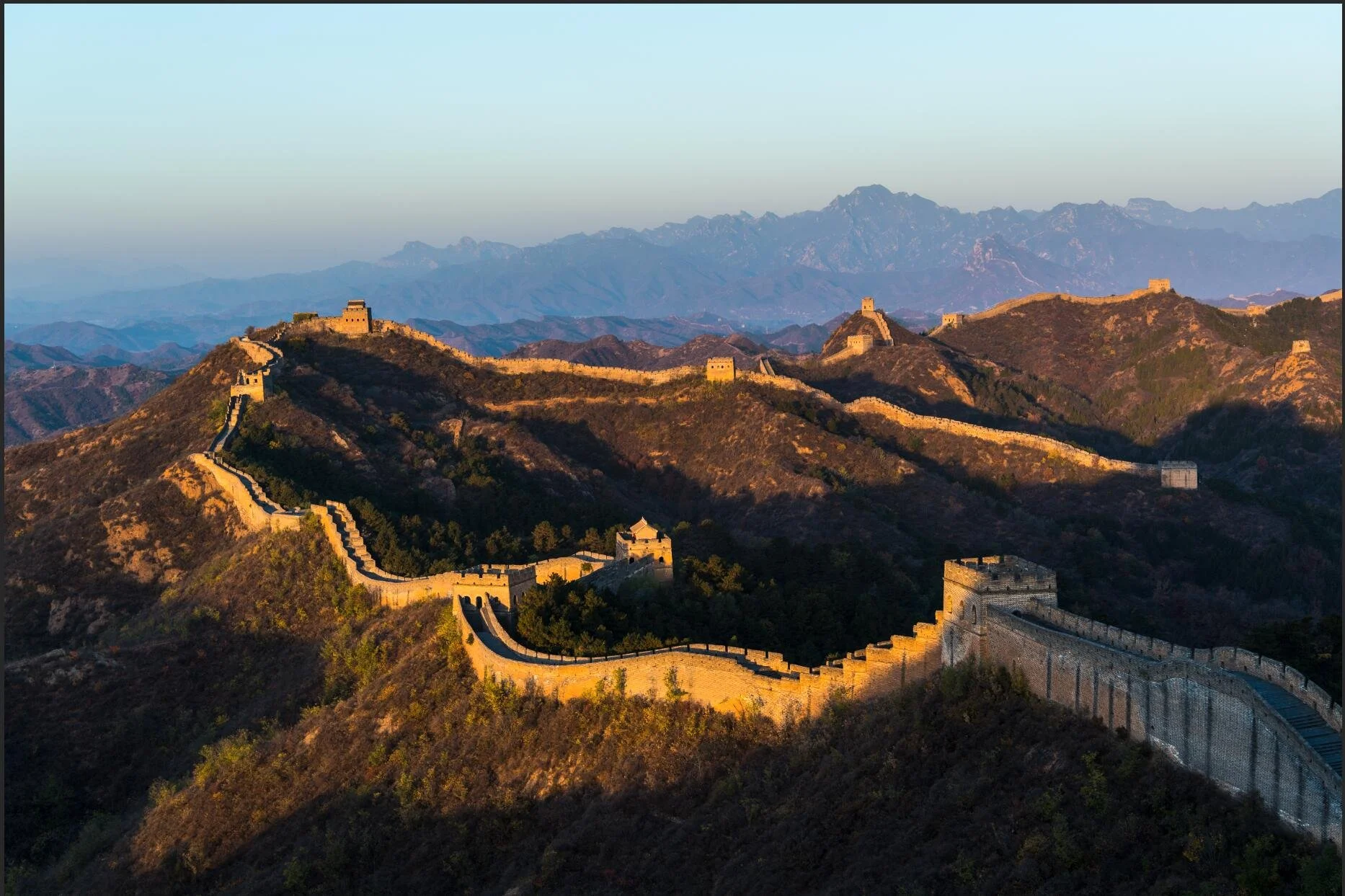 The Great Wall of China winding over mountain ridges during sunset.