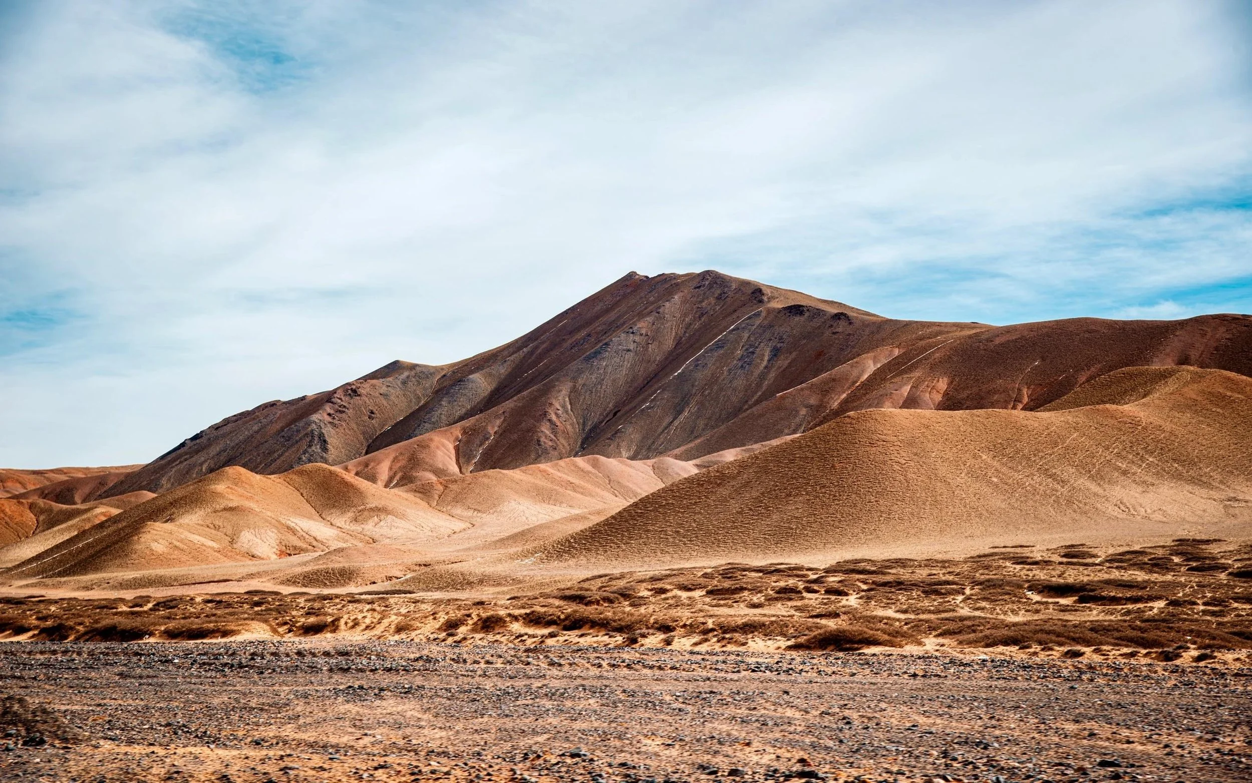Brown, layered desert mountains under a partly cloudy sky.