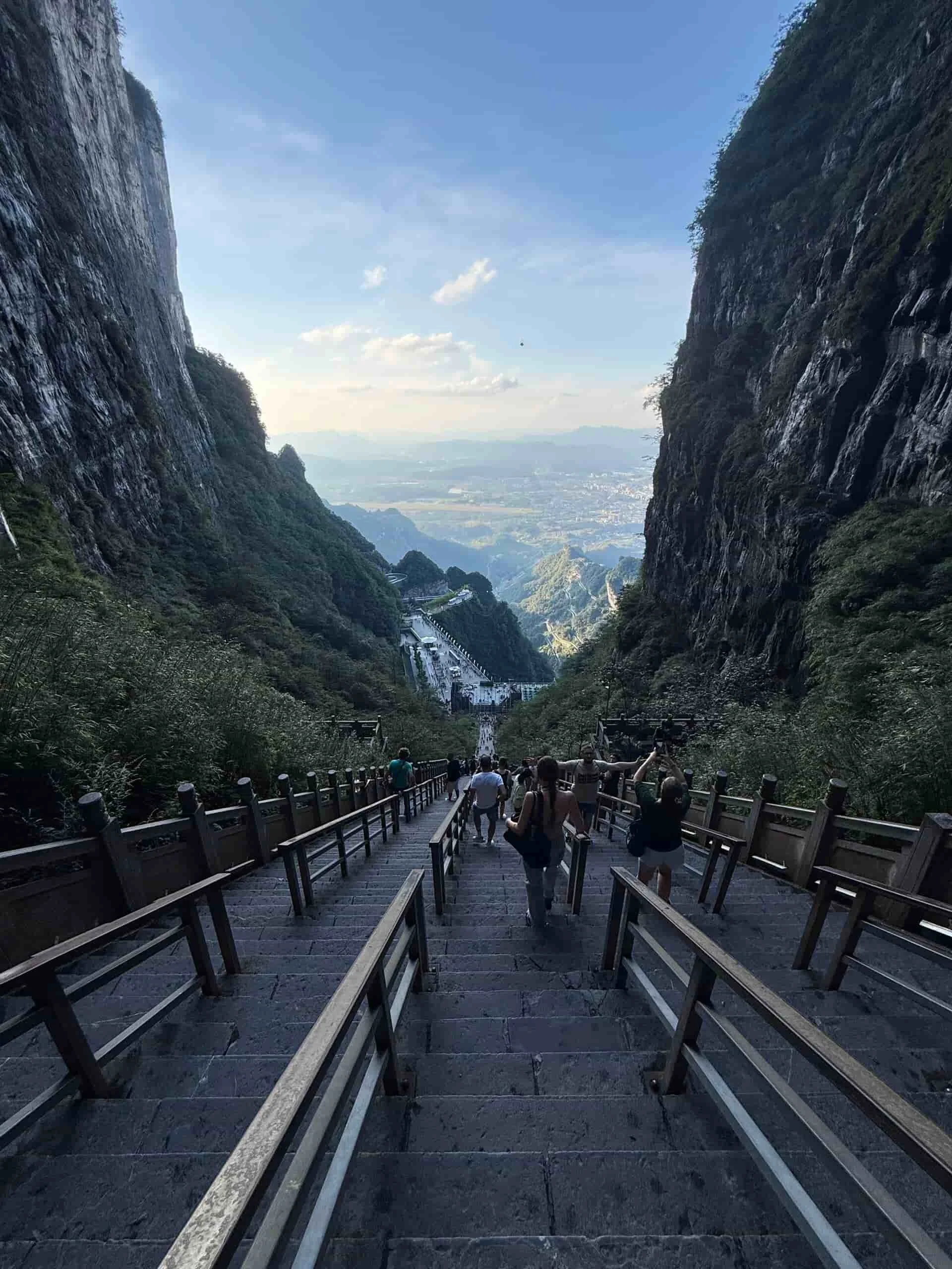 Person standing on a wooden viewing platform overlooking lush green mountains and towering rock formations shrouded in mist in Huangshan, China.