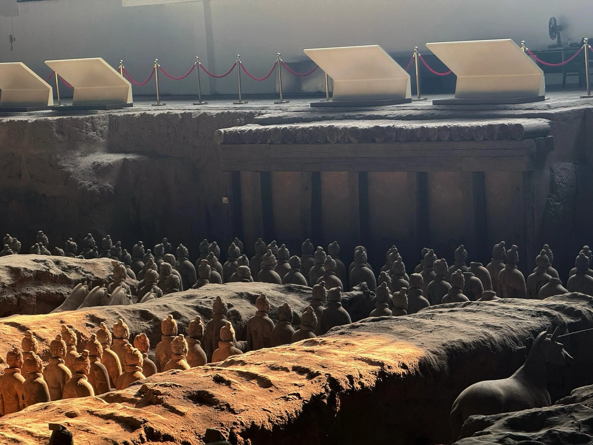 Ancient terracotta Army statues in a large underground chamber with excavated rocks and dim lighting.