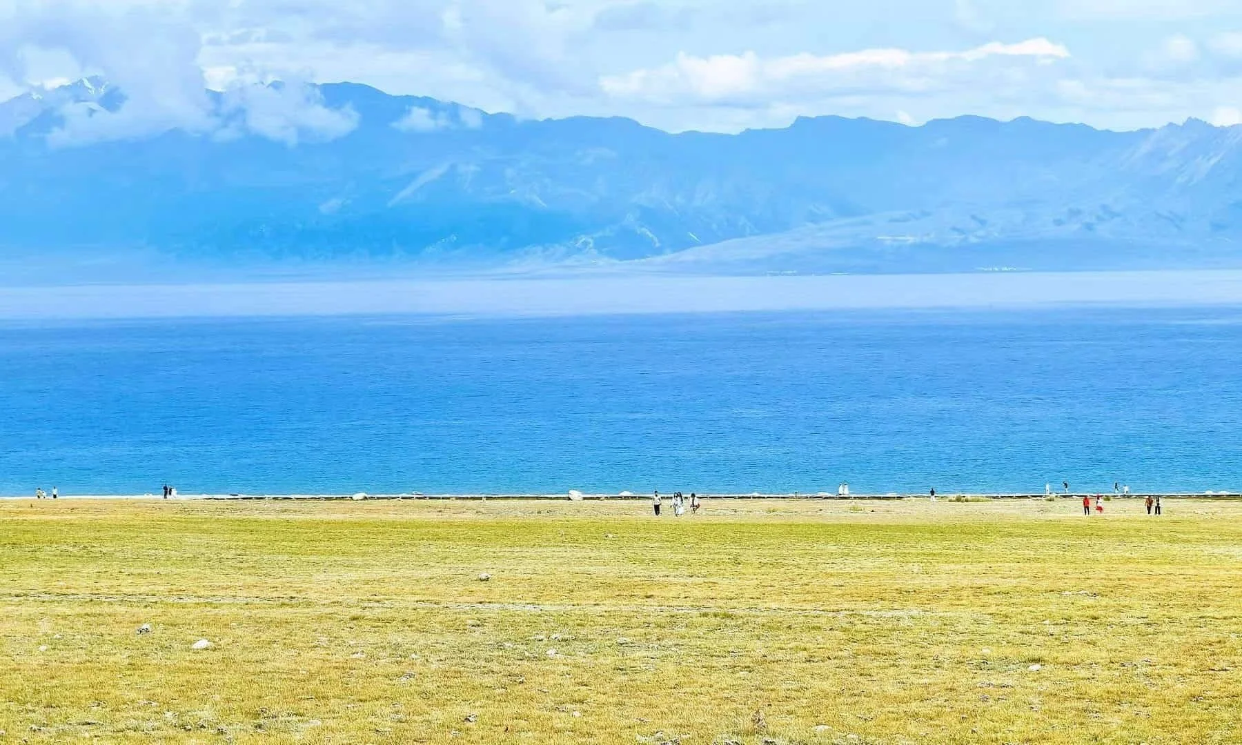 A scenic view of a large blue reservoir surrounded by lush green hills and steep mountains with rocky cliffs.