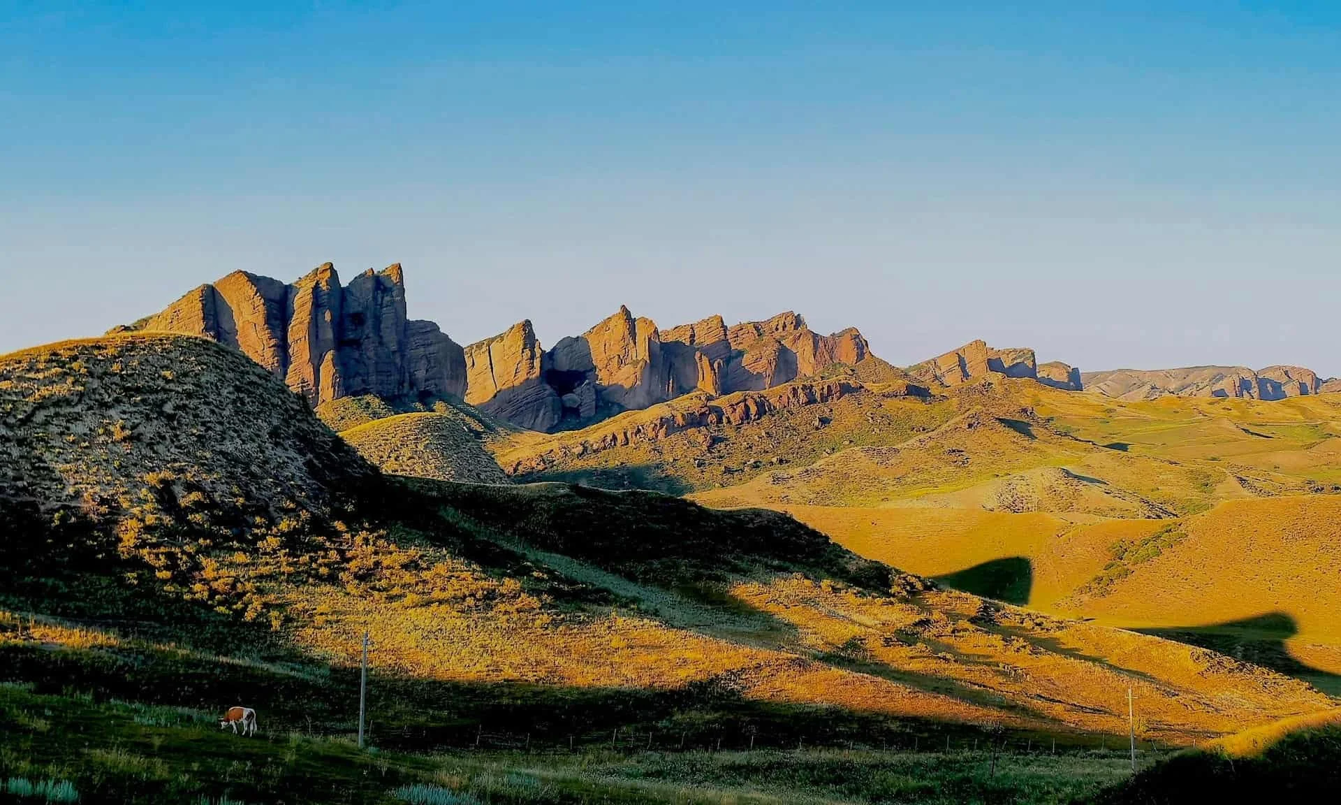 Colorful mountain range with sharp peaks, including one prominent pointed peak, under a clear blue sky.