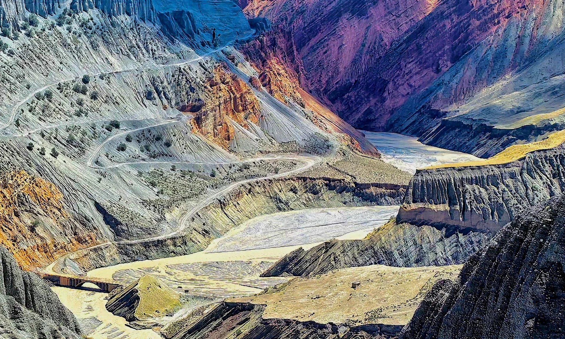 Colorful mountainous canyon with winding road and river visible in the valley.