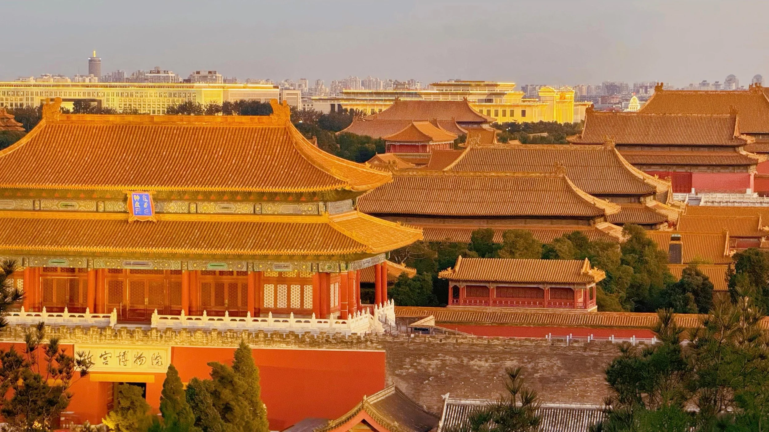Traditional Chinese buildings with ornate roofs and modern city skyline in the background during sunset.