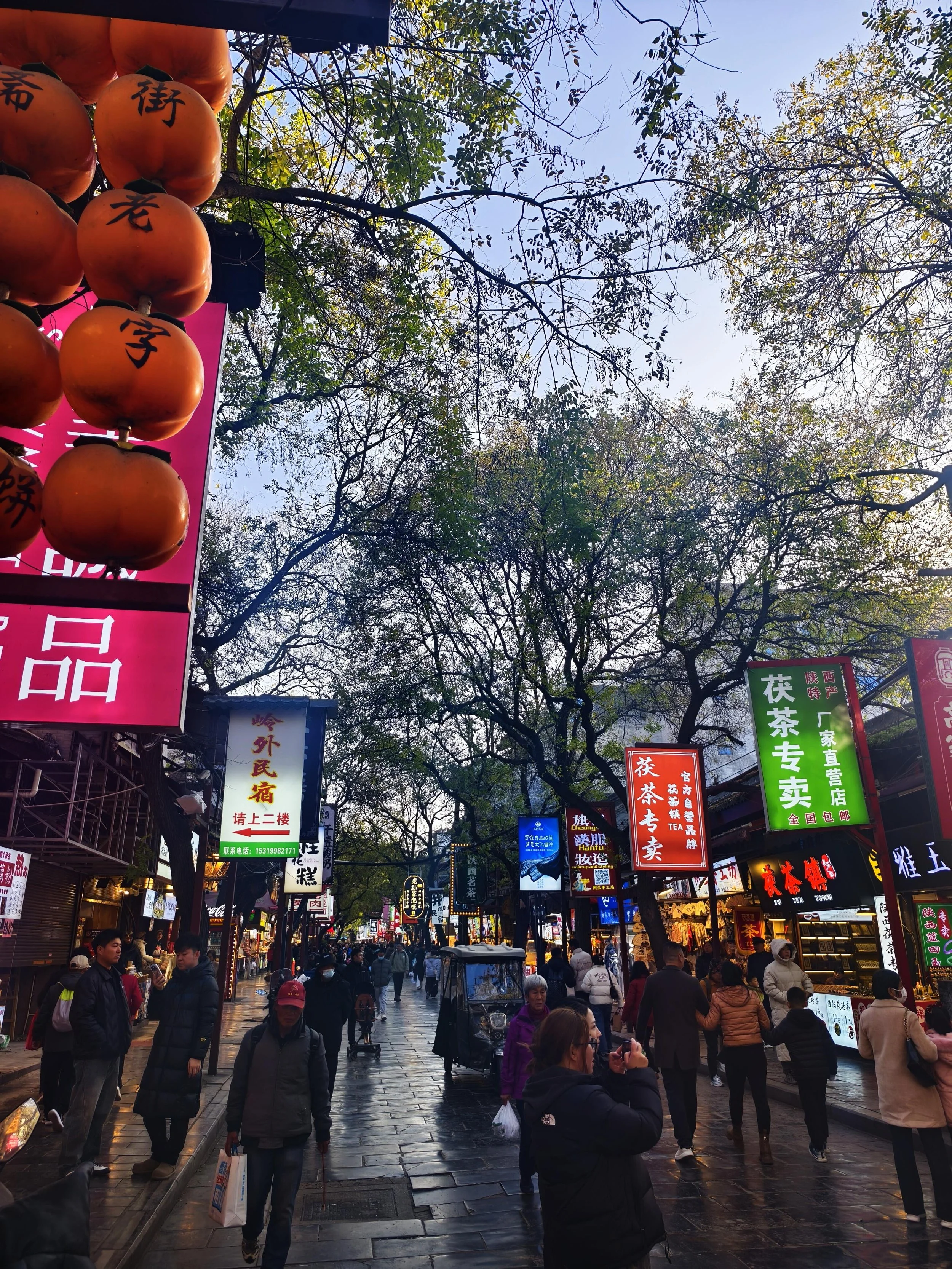 A busy backstreet in Xi'an at dusk lined with Chinese-only shop signs for tea houses and guesthouses — the everyday signage environment foreign visitors navigate in China
