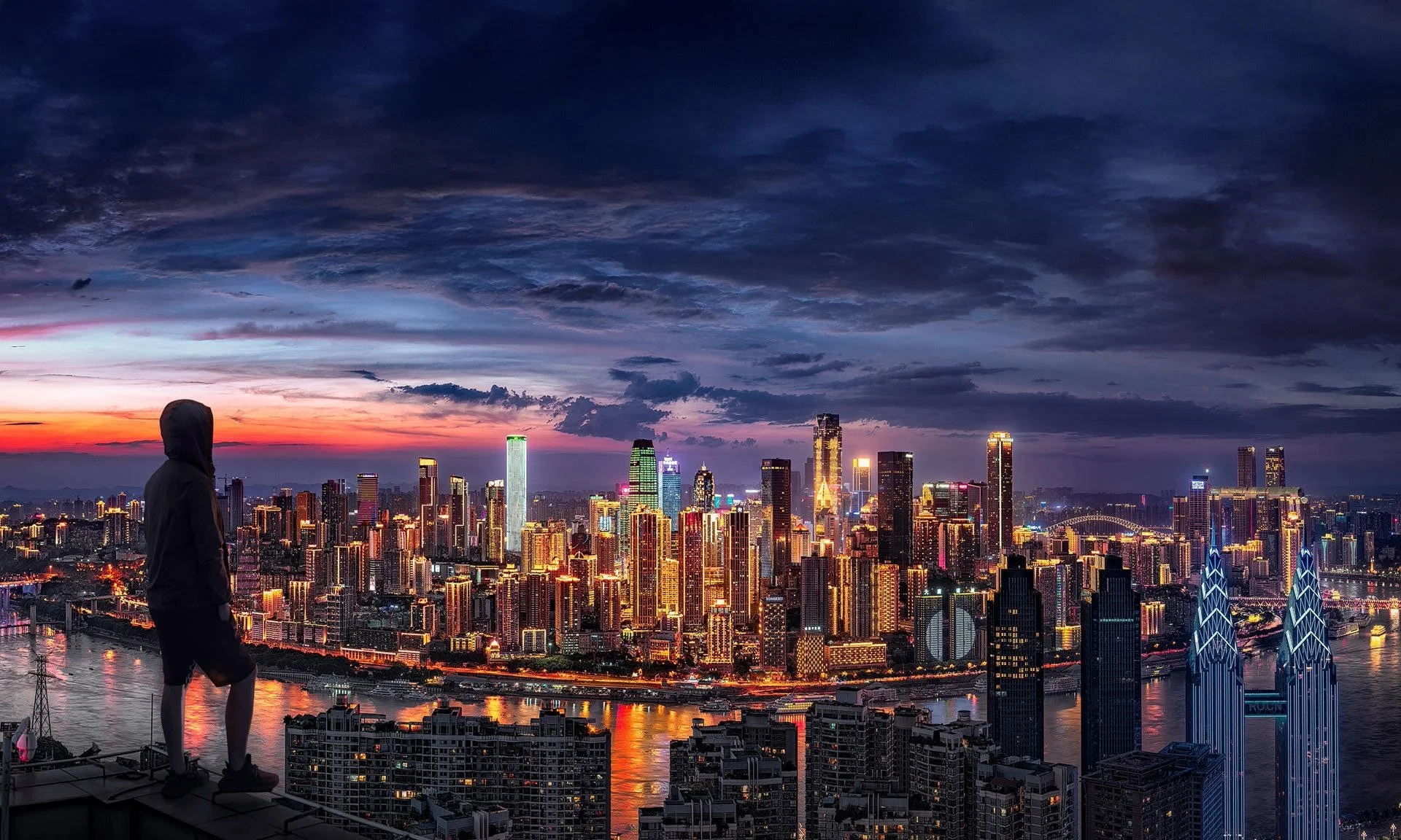 A person in a hoodie stands on a high ledge overlooking a city skyline at dusk. The city is filled with brightly lit skyscrapers, and the sky is a mix of dark clouds and colorful sunset hues.