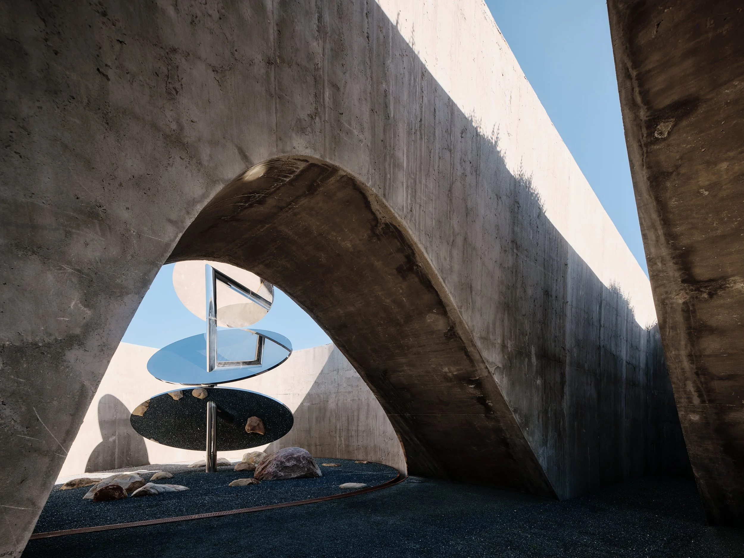 A modern outdoor space with concrete arches, a slide, and seating areas, under a clear blue sky.