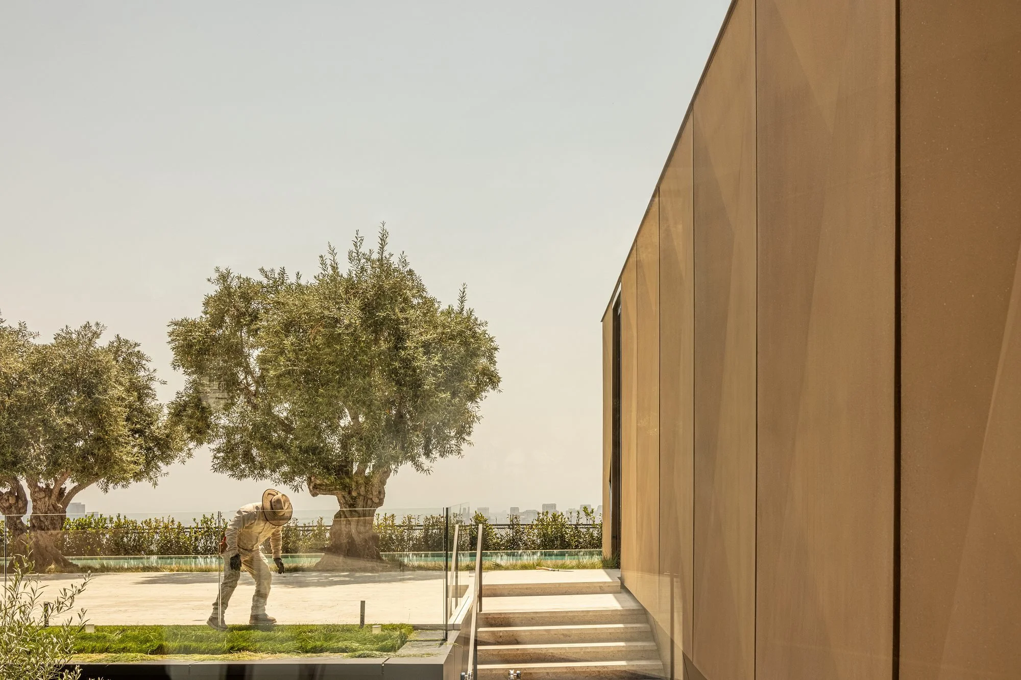 A construction worker wearing a helmet and protective gear working outdoors near large trees and a modern building.