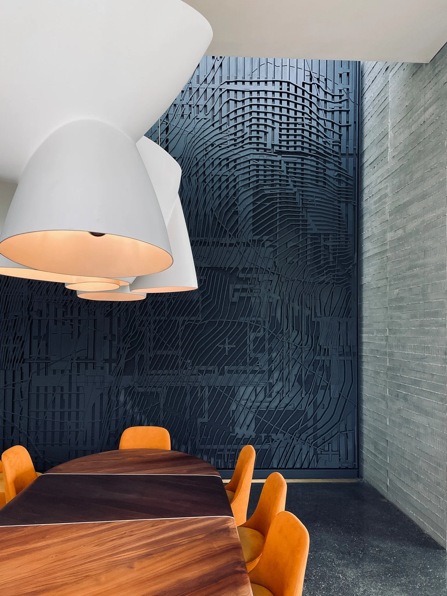 Custom sculptural wall with integrated lighting, wood tables, and textured concrete in a Donaldson + Partners interior.