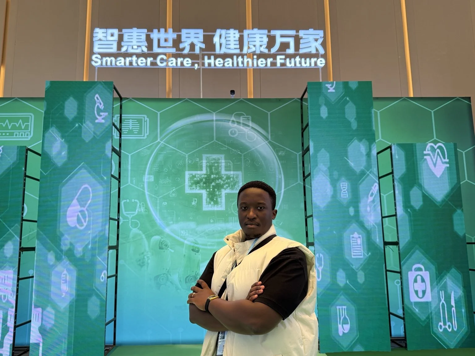 A man standing with arms crossed in front of a digital health care display with medical icons, and a sign above that says 'Smarter Care, Healthier Future' in English and Chinese.