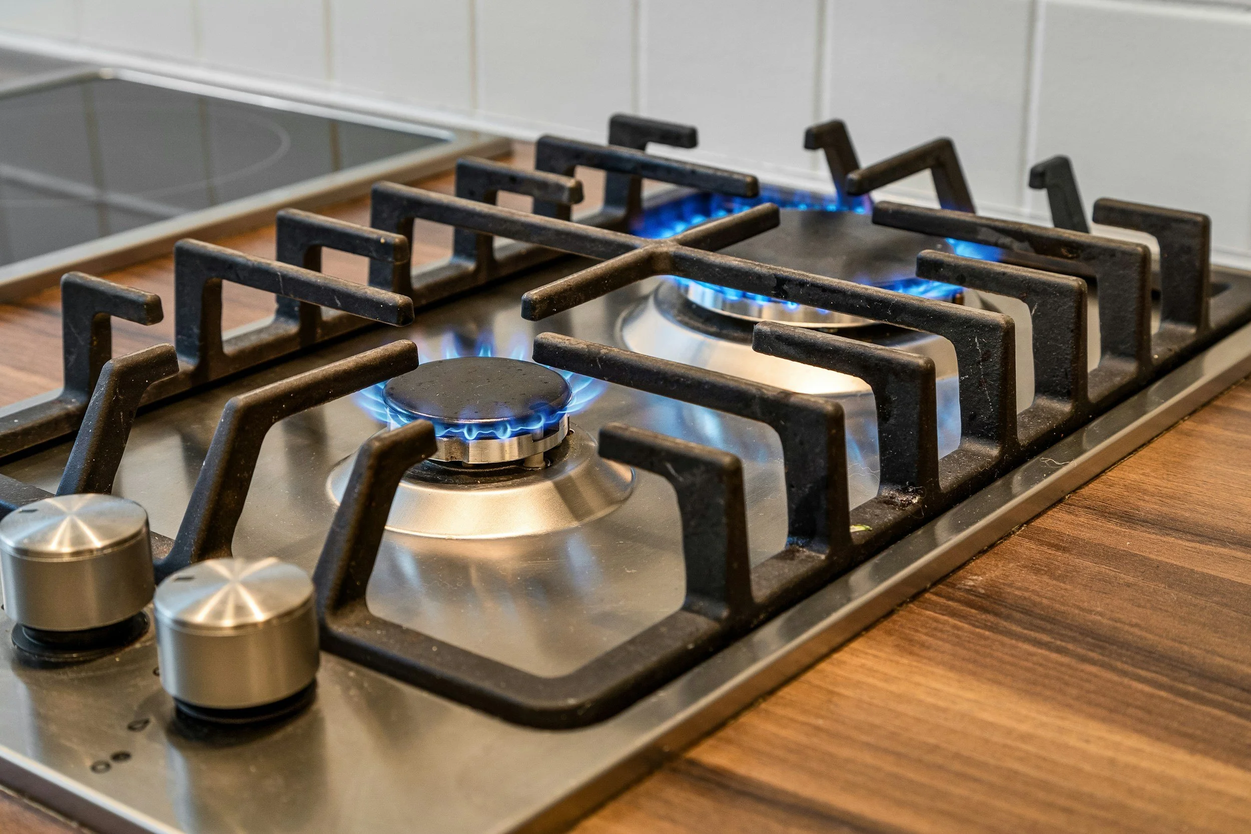 A stainless steel gas stove with five burners, four of which are turned on with blue flames visible, on a wooden countertop in a kitchen.