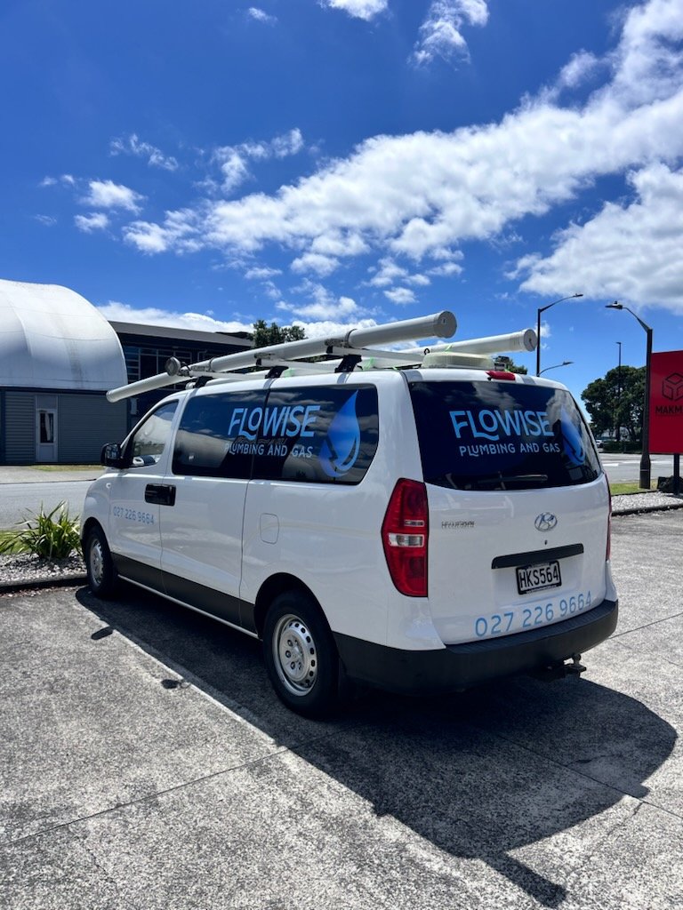 White service van with 'Flowise Plumbing and Gas' logos on the side and back, parked in a parking lot on a sunny day with a blue sky and scattered clouds.